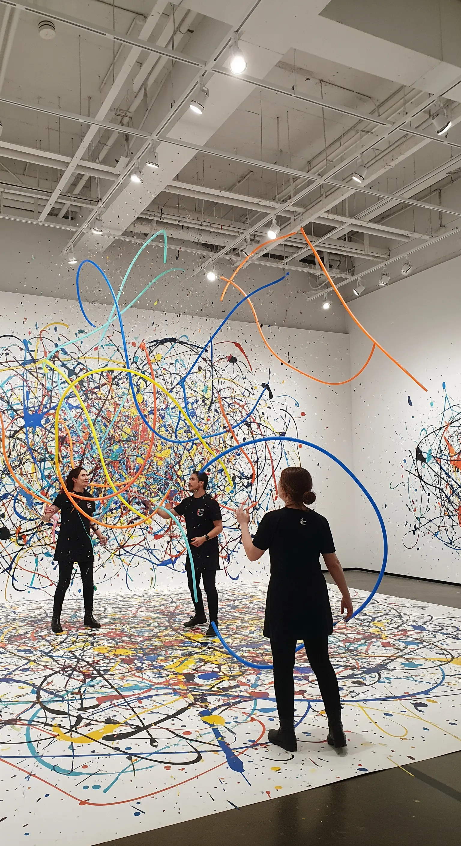 Persone che creano un'opera di action painting lanciando palloncini colorati su una tela gigante.