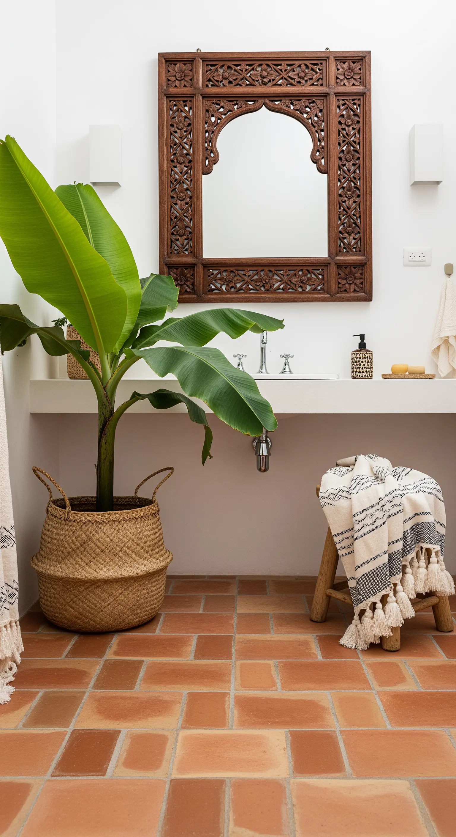 Bagno con pavimento in cotto, specchio in legno intagliato e una pianta di banano.