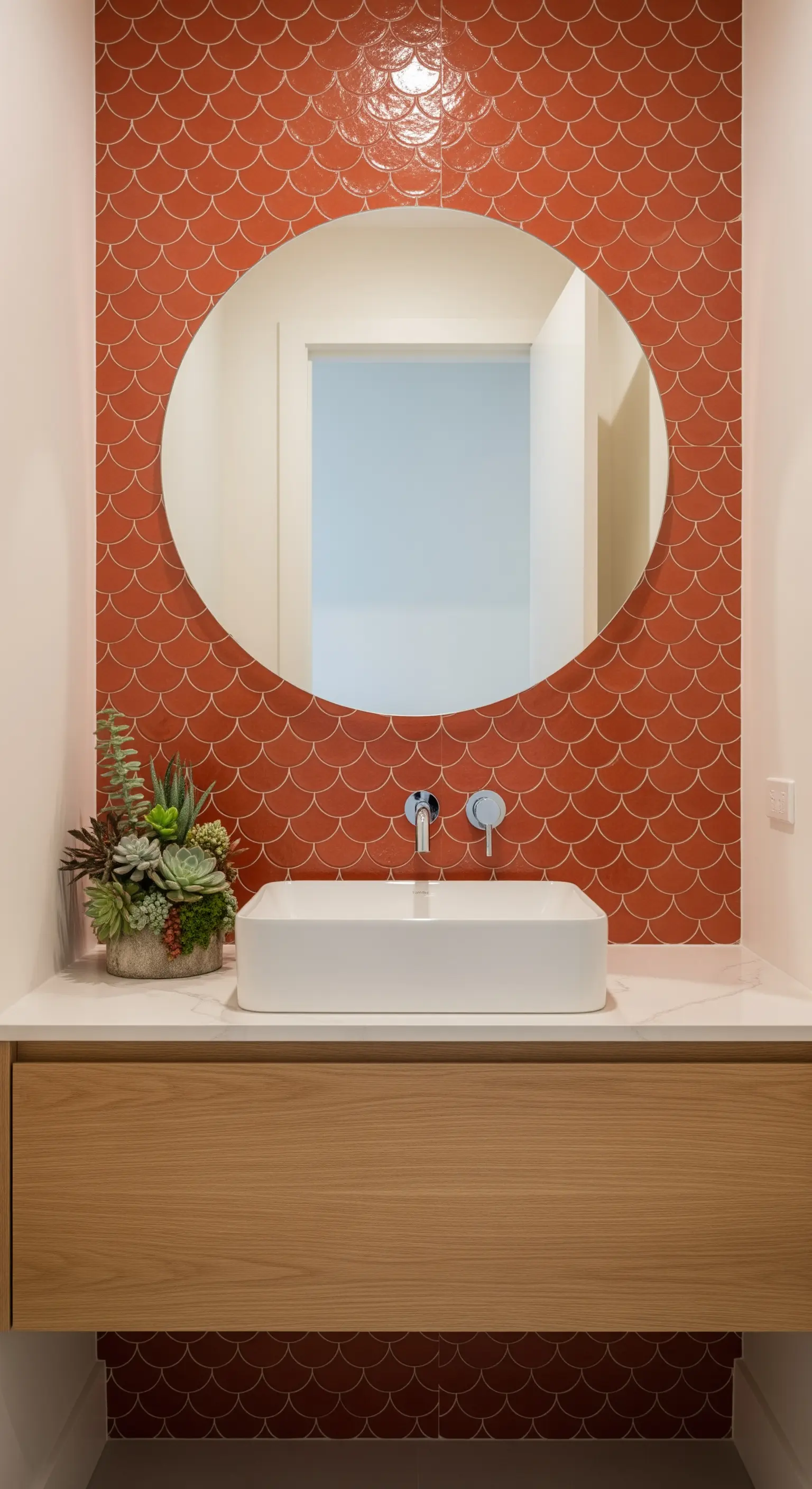 Dettaglio di un lavabo con paraschizzi in piastrelle terracotta a forma di squama e specchio rotondo.