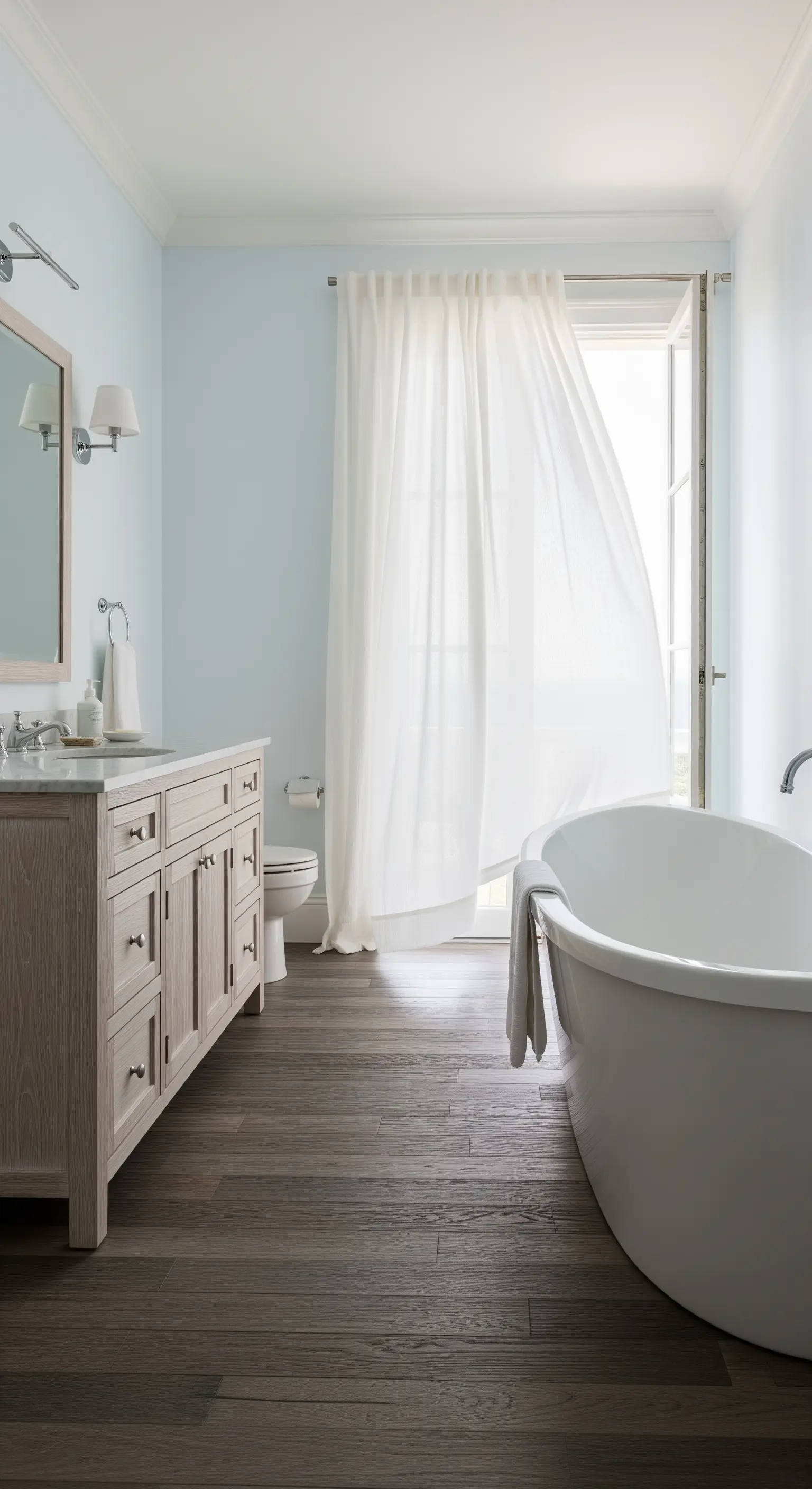 Bagno luminoso con parquet grigio-marrone, pareti azzurro polvere e una tenda bianca leggera che fluttua.