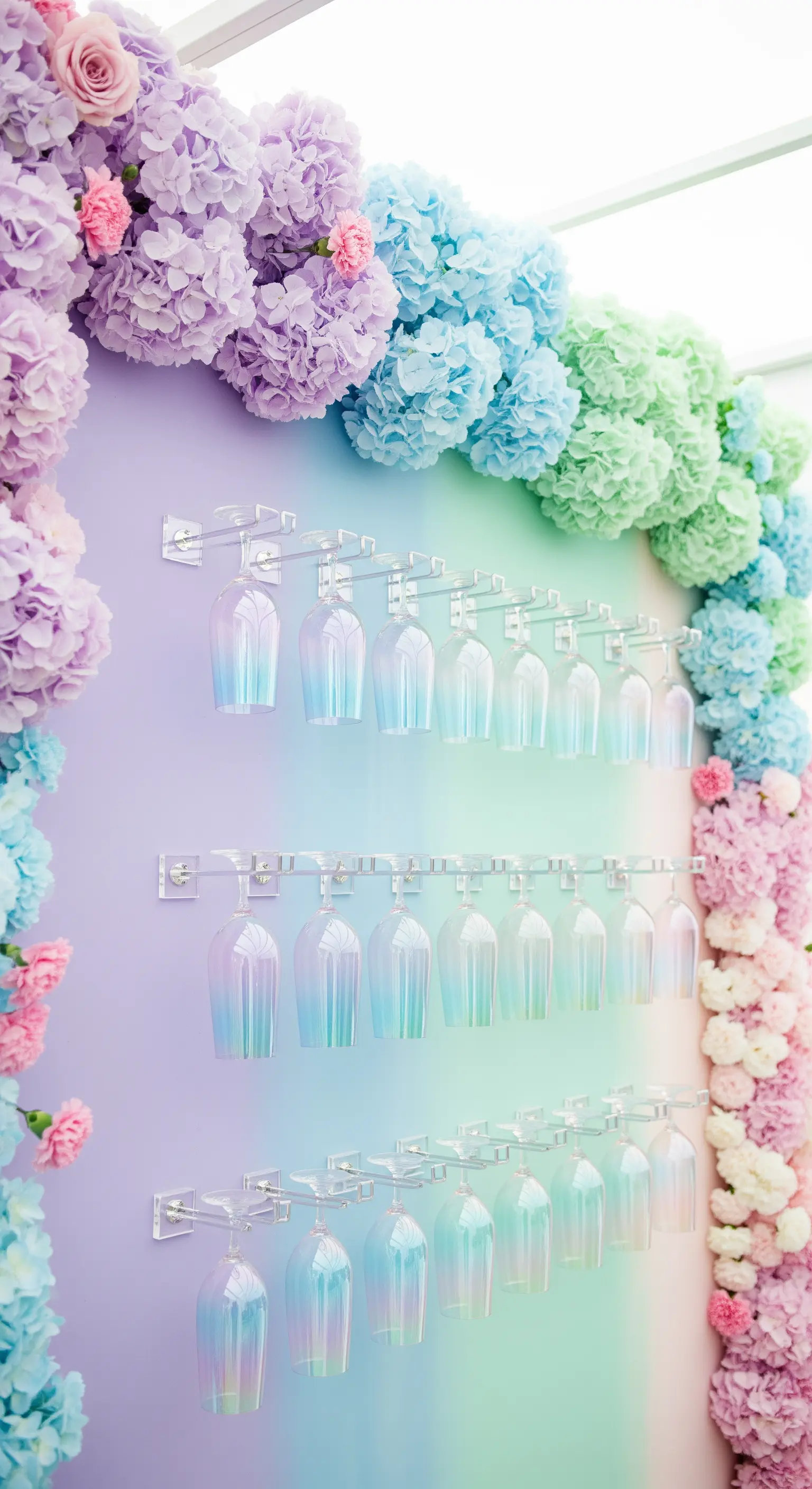 Parete sfumata arcobaleno pastello, arco di ortensie colorate e calici iridescenti.