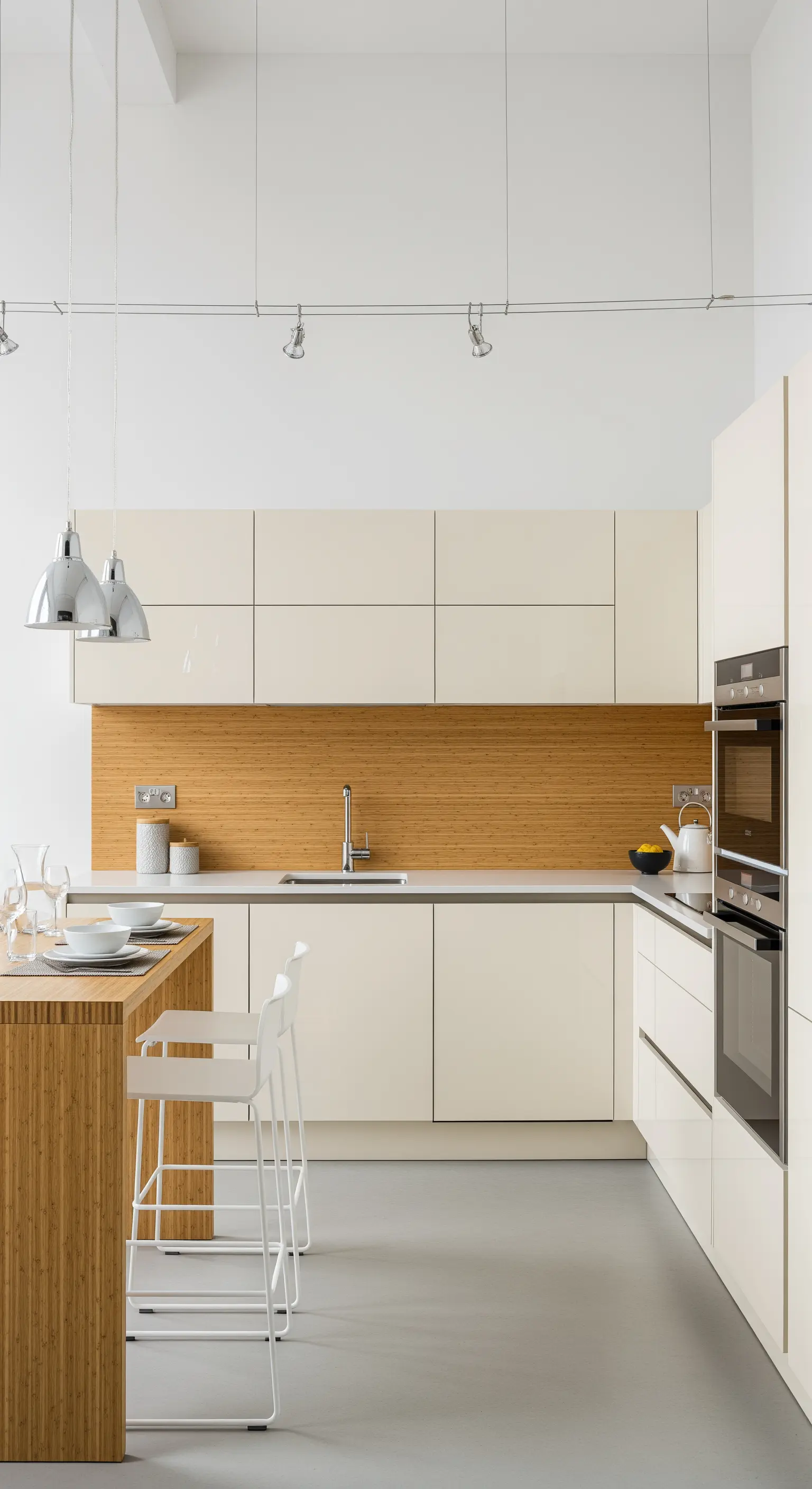 Cucina moderna con mobili laccati color crema e un paraschizzi in bambù orizzontale.