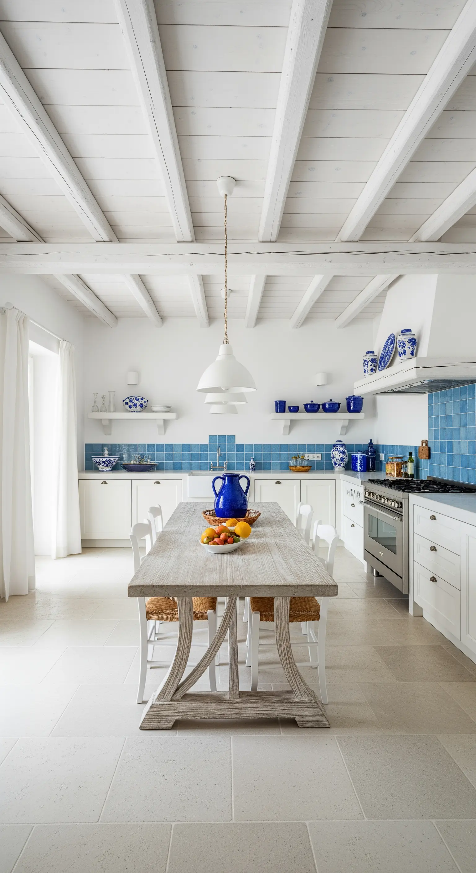 Cucina bianca con travi a vista dipinte, piastrelle blu e tavolo in legno chiaro.
