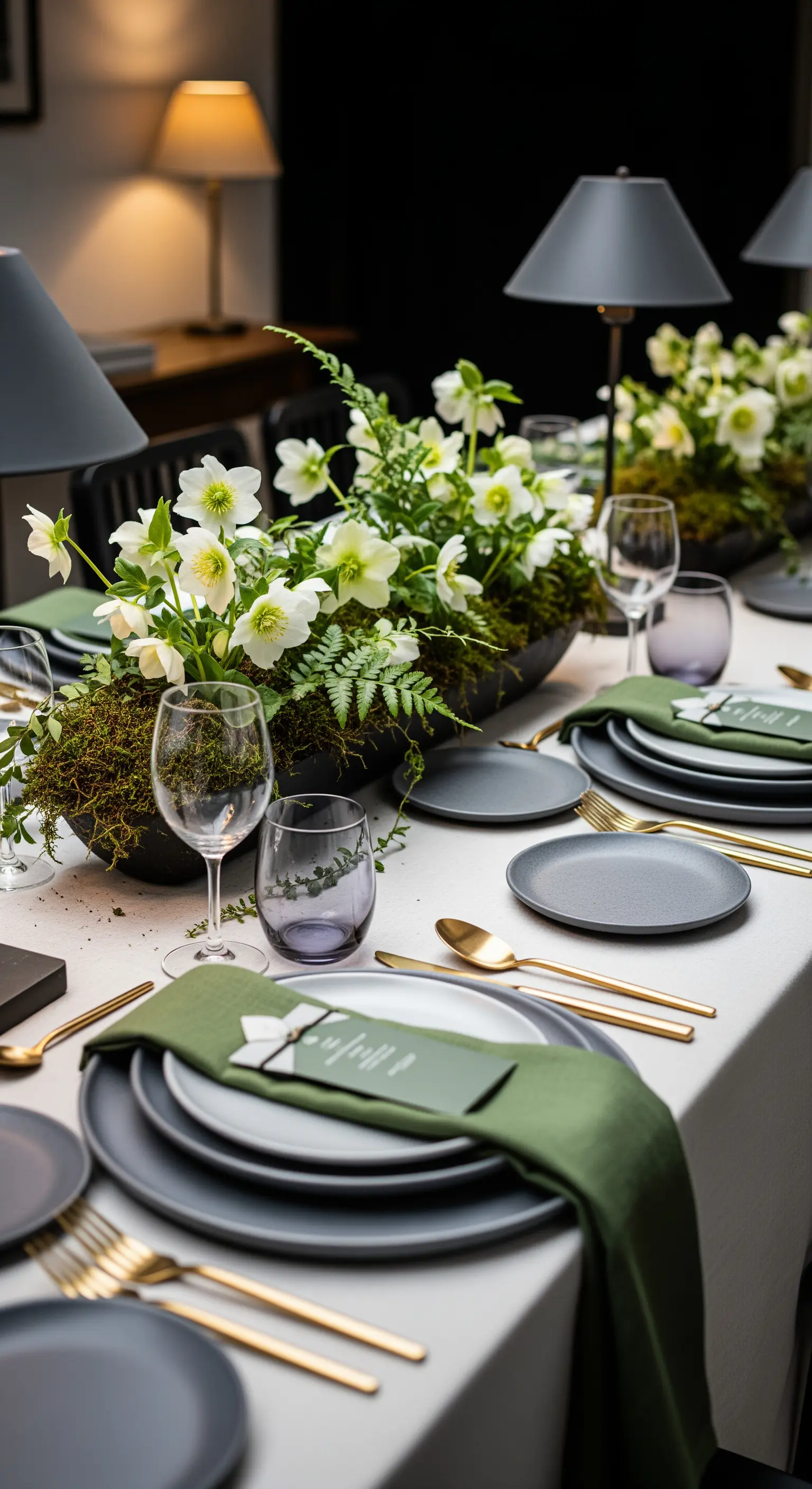 Tavola moderna con piatti grigi, tovaglioli verde oliva, posate dorate e centrotavola naturale.