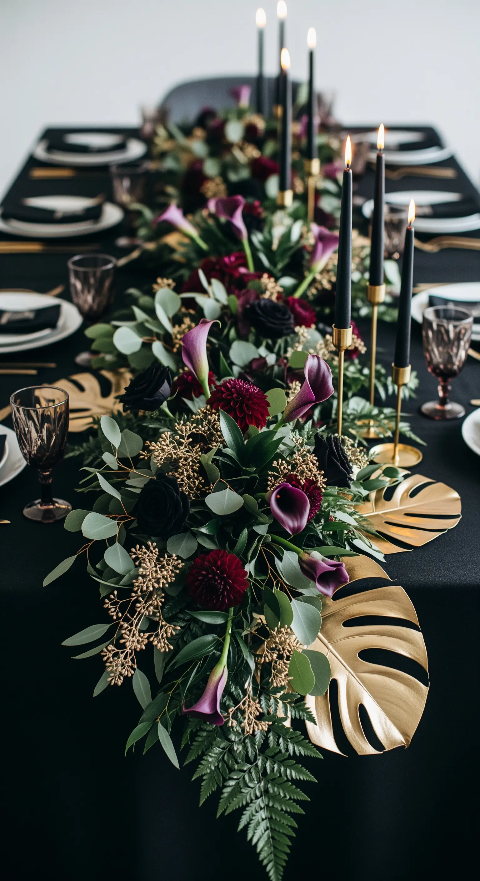 Centrotavola floreale con fiori bordeaux e viola, foglie dorate e candele nere.