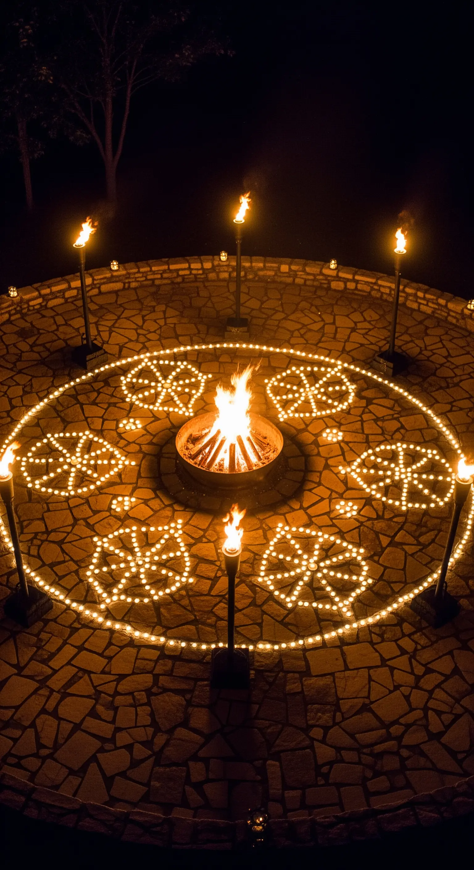 Braciere circondato da motivi geometrici realizzati con candele su una pavimentazione in pietra.