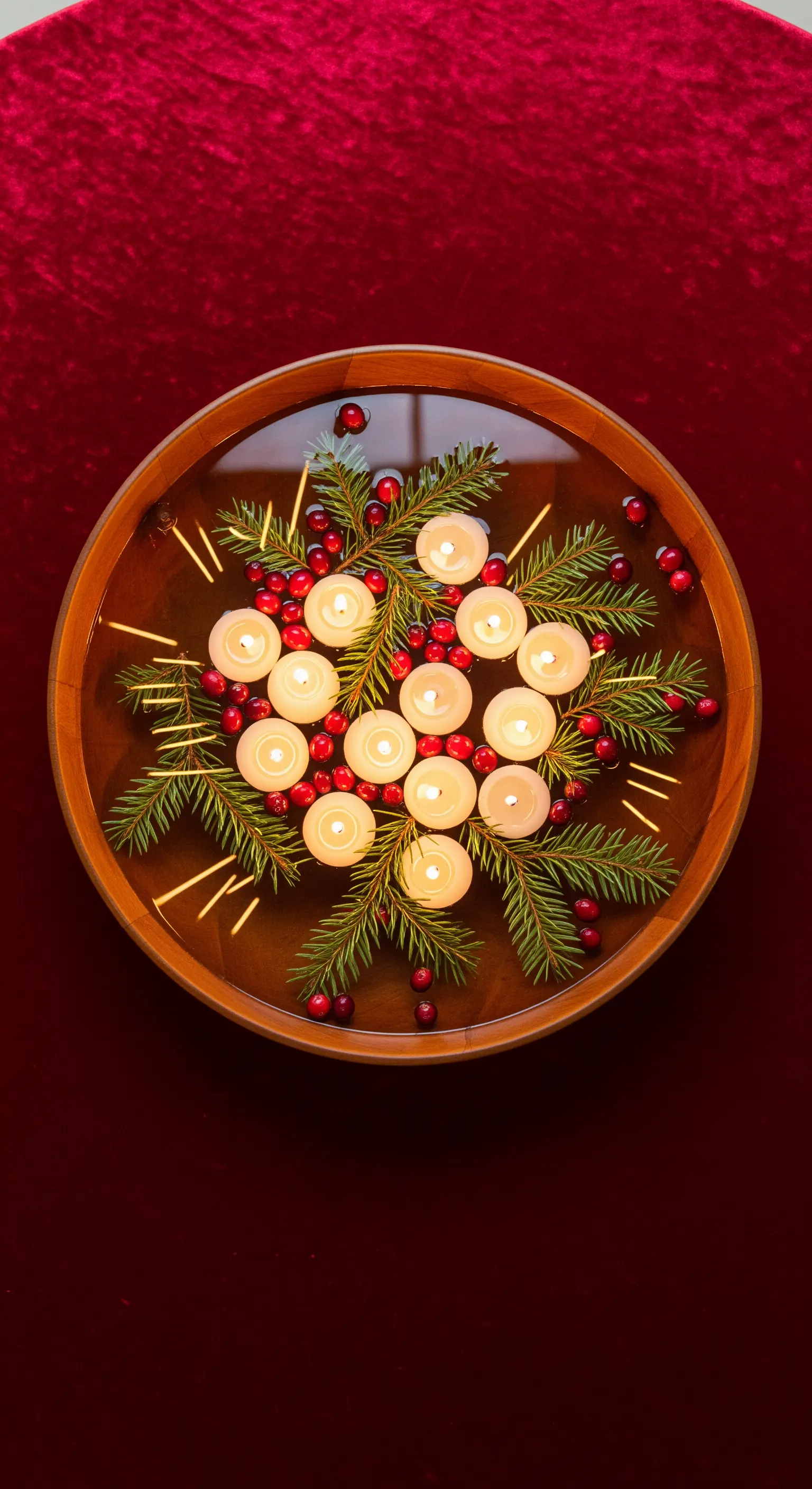 Centrotavola con candele galleggianti, pino e bacche rosse in una ciotola di legno.