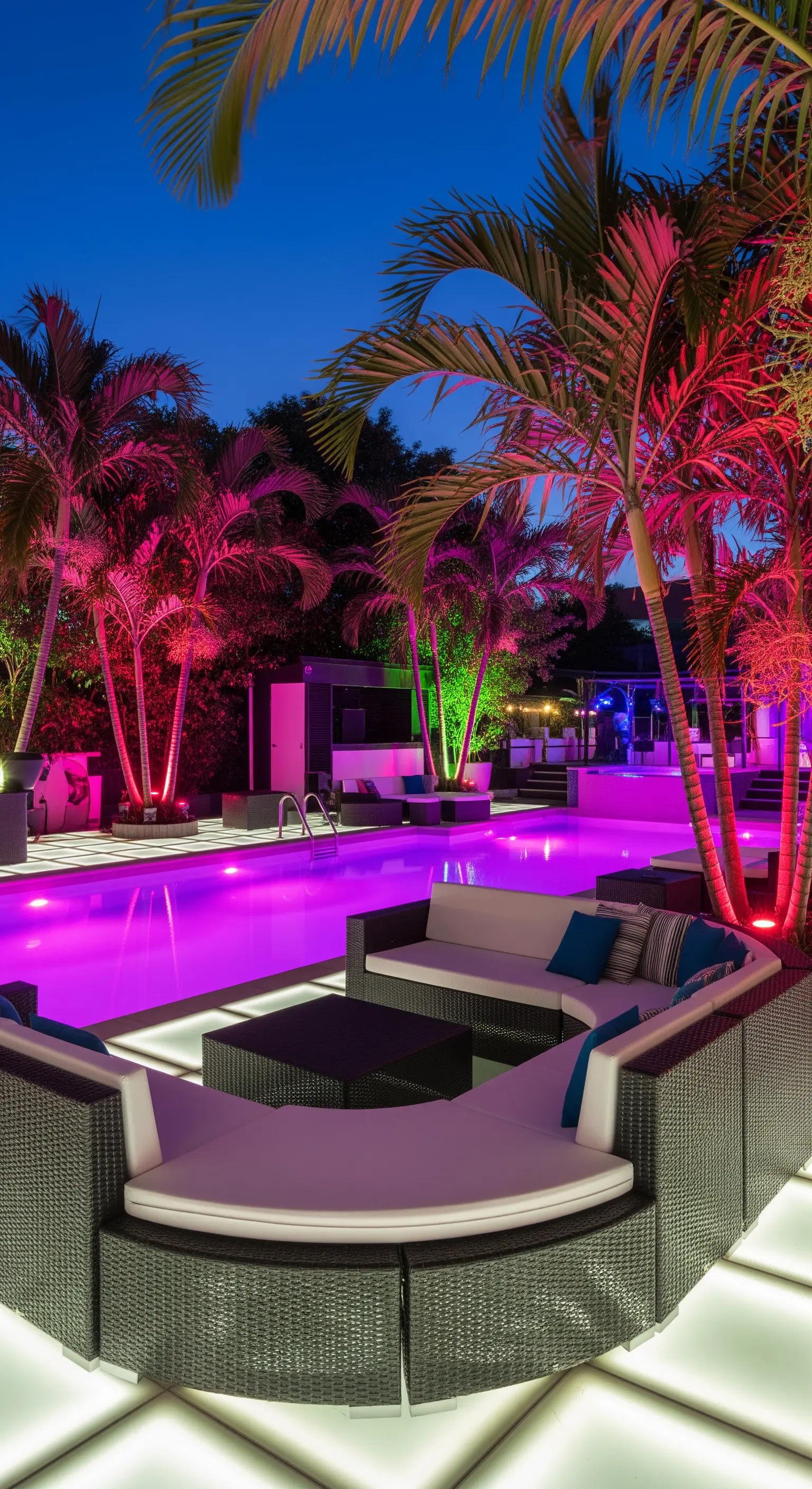 Festa a bordo piscina con palme illuminate di rosa e verde e sedute bianche luminose.