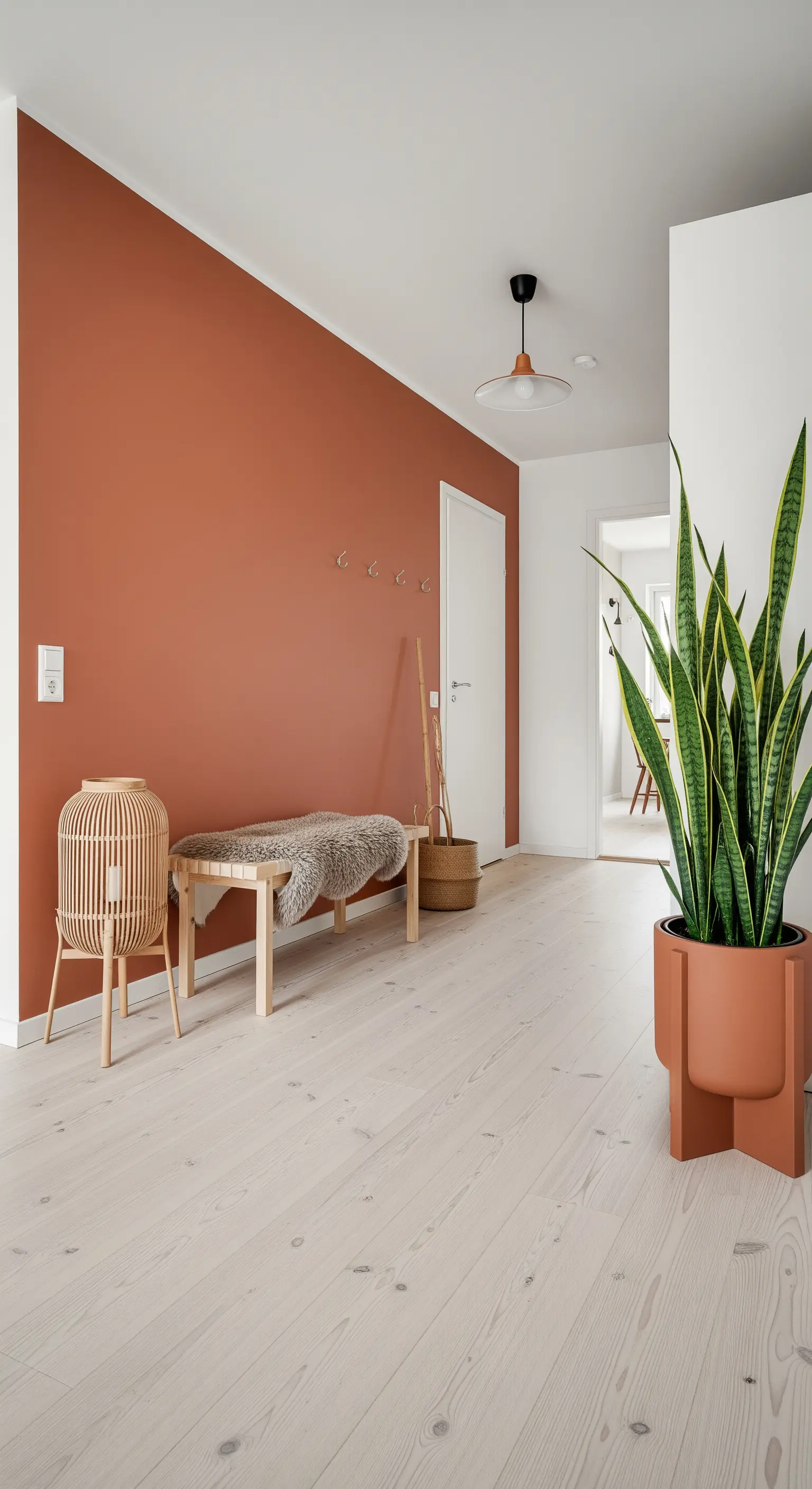 Ingresso in stile scandinavo con parete d'accento terracotta, pavimento in legno chiaro e panca minimalista.