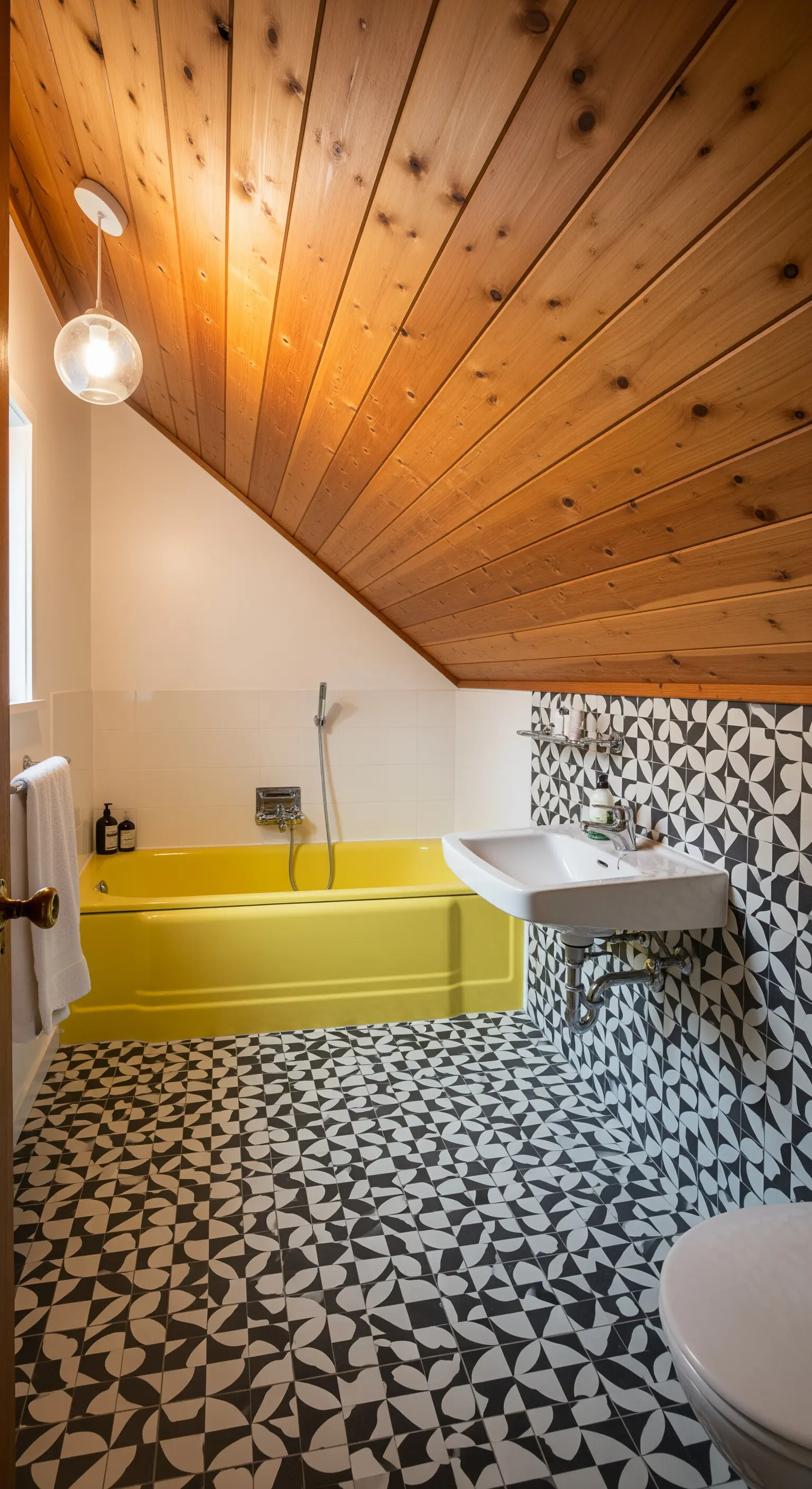 Bagno in mansarda con soffitto in legno, piastrelle optical e vasca gialla.