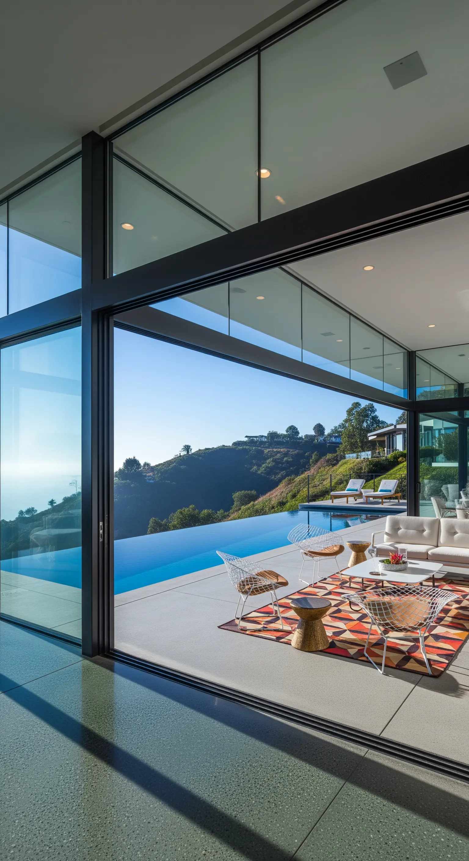 Soggiorno che si apre su un patio con piscina a sfioro grazie a vetrate scorrevoli.