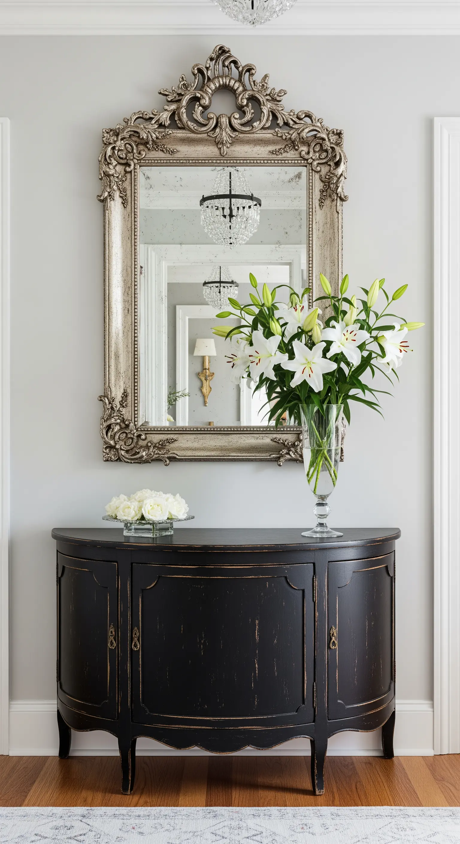 Consolle nera a mezzaluna con finitura usurata, sormontata da un grande specchio barocco argento.