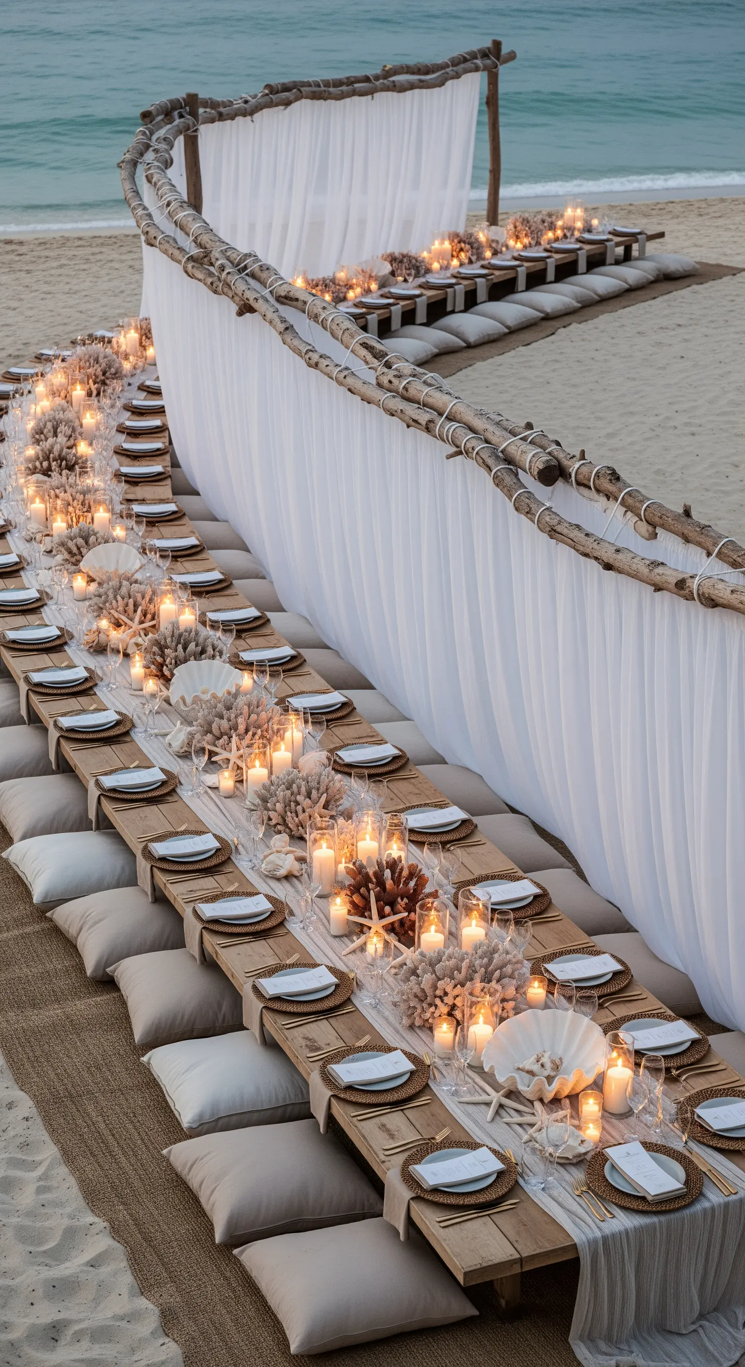 Lunga tavolata bassa sulla spiaggia per una cena, con cuscini, candele e decorazioni marine.
