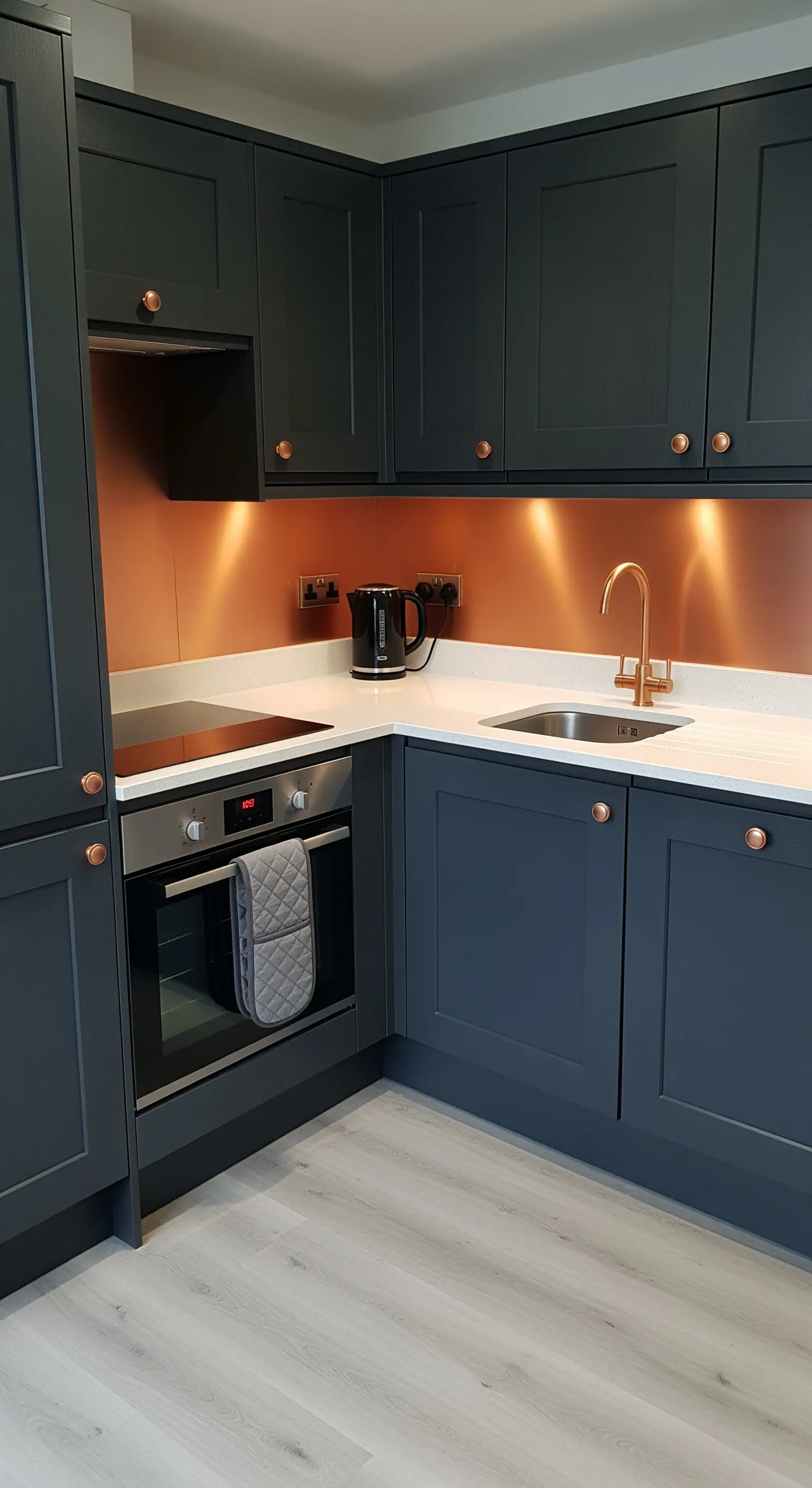 Cucina compatta con mobili blu scuro e un paraschizzi in rame luminoso.