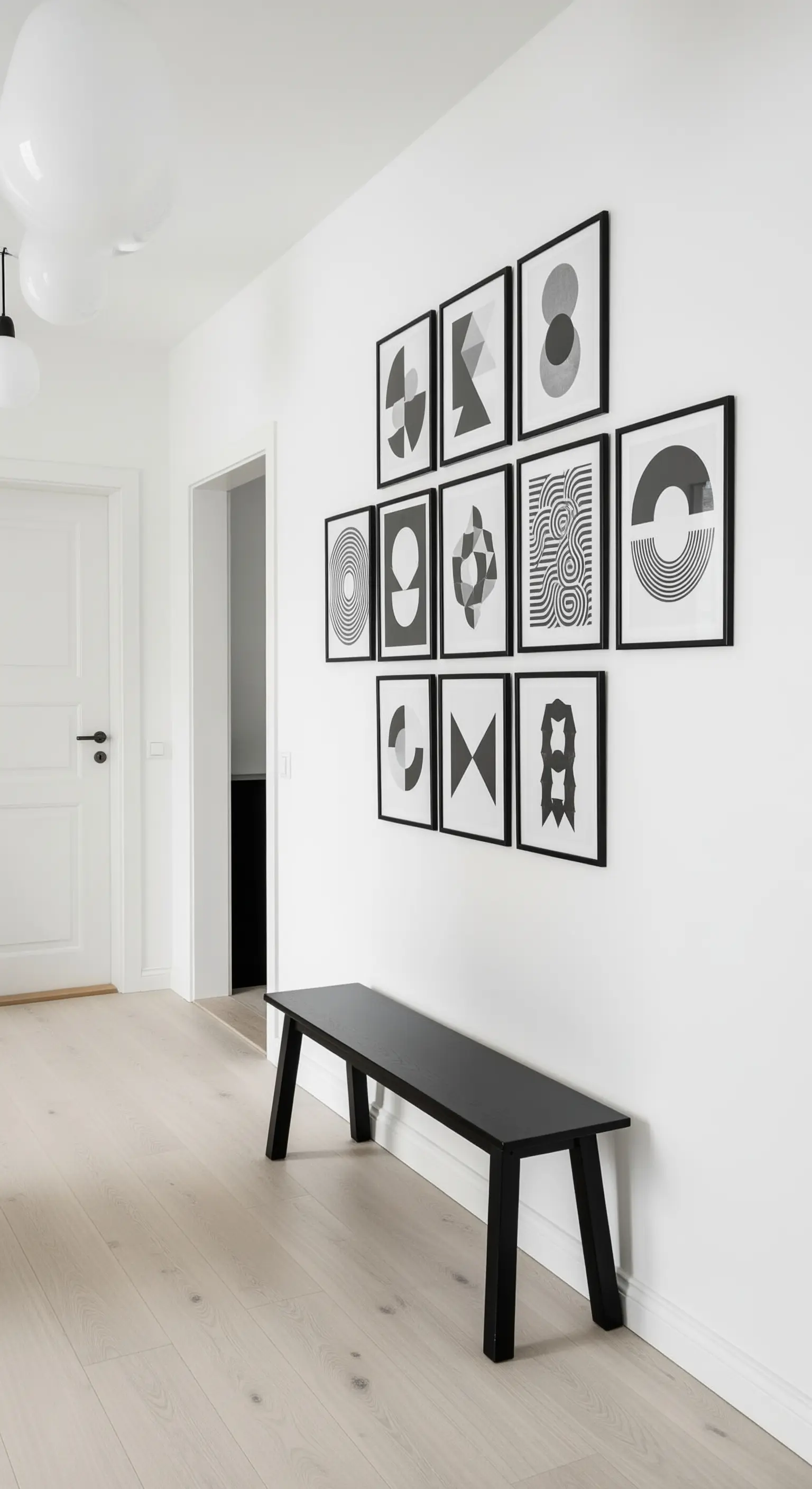 Galleria a parete con stampe geometriche in bianco e nero disposte a griglia sopra una panca nera.