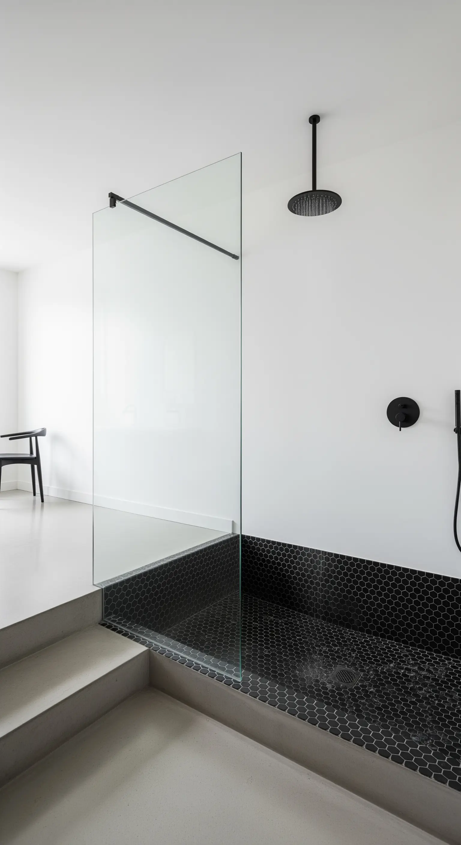 Doccia a livello ribassato con mosaico esagonale nero e parete in vetro.