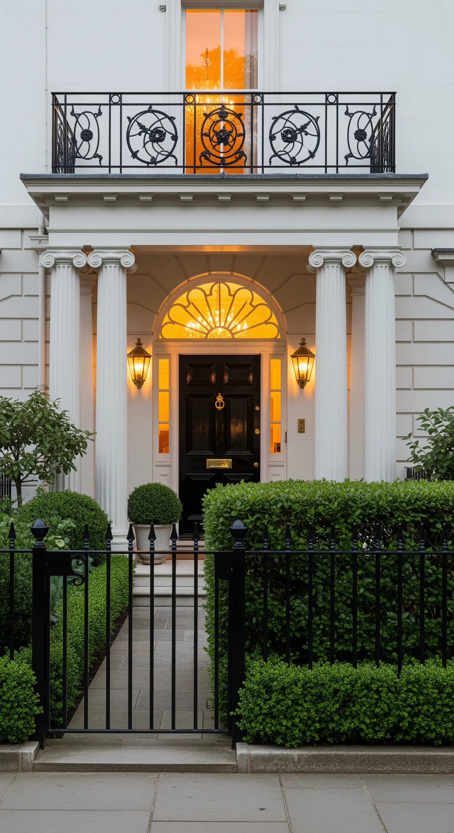 Ingresso di una townhouse londinese con portico a colonne, recinzione nera e siepi curate.