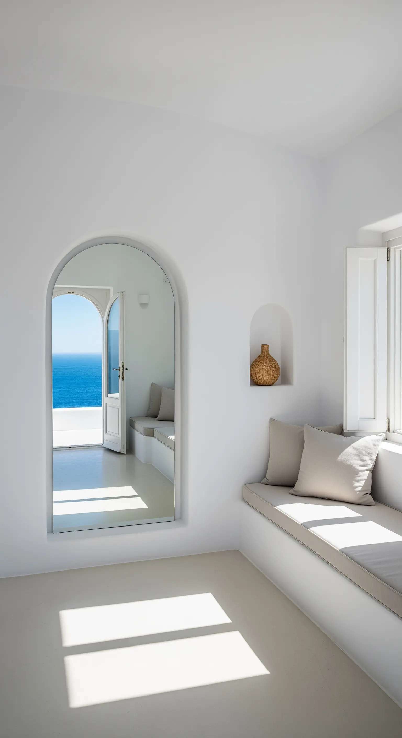 Specchio ad arco in una stanza bianca che riflette una porta aperta sul mare blu.