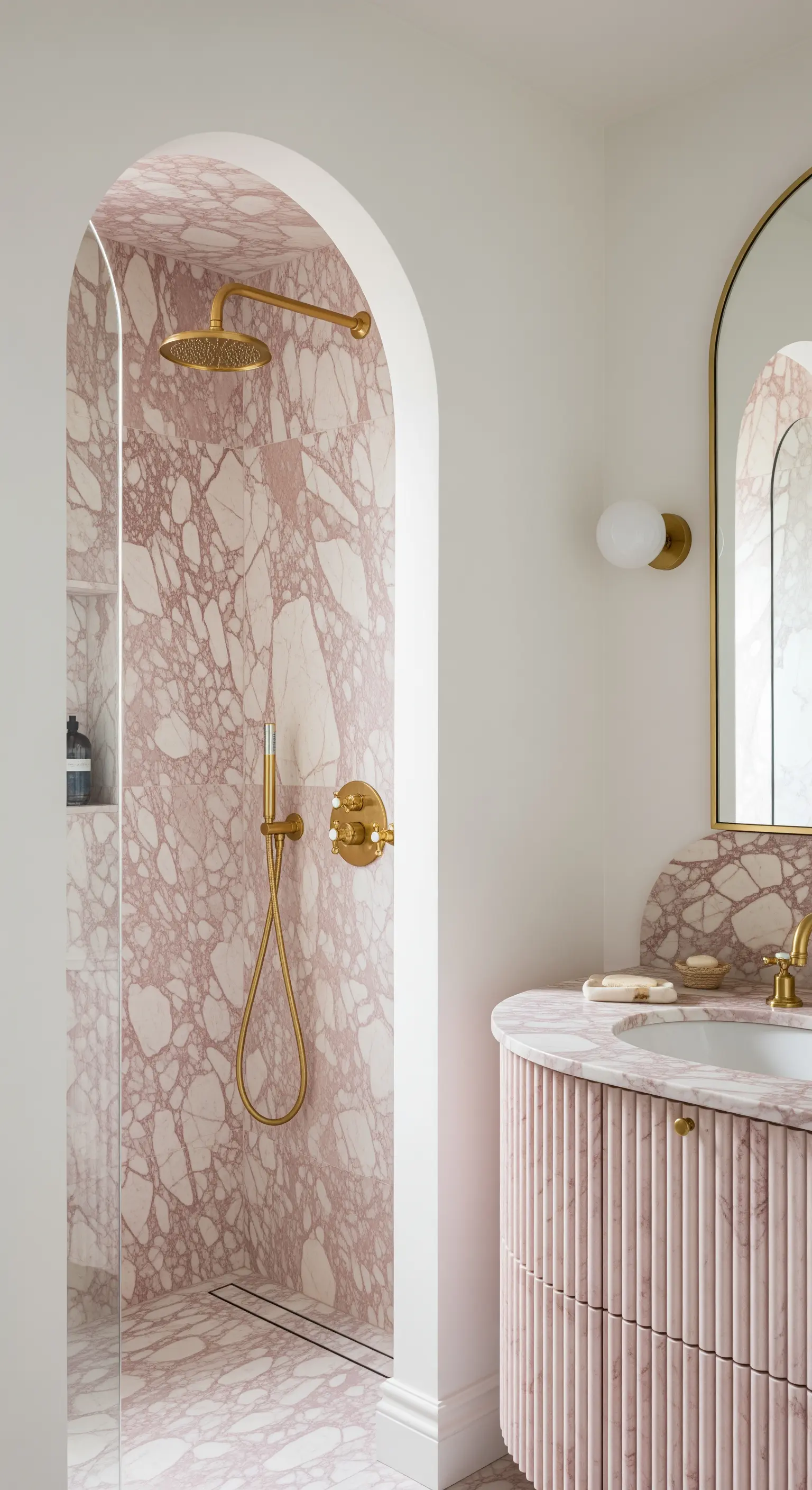 Bagno con marmo rosa, doccia con ingresso ad arco e mobile lavabo curvo.