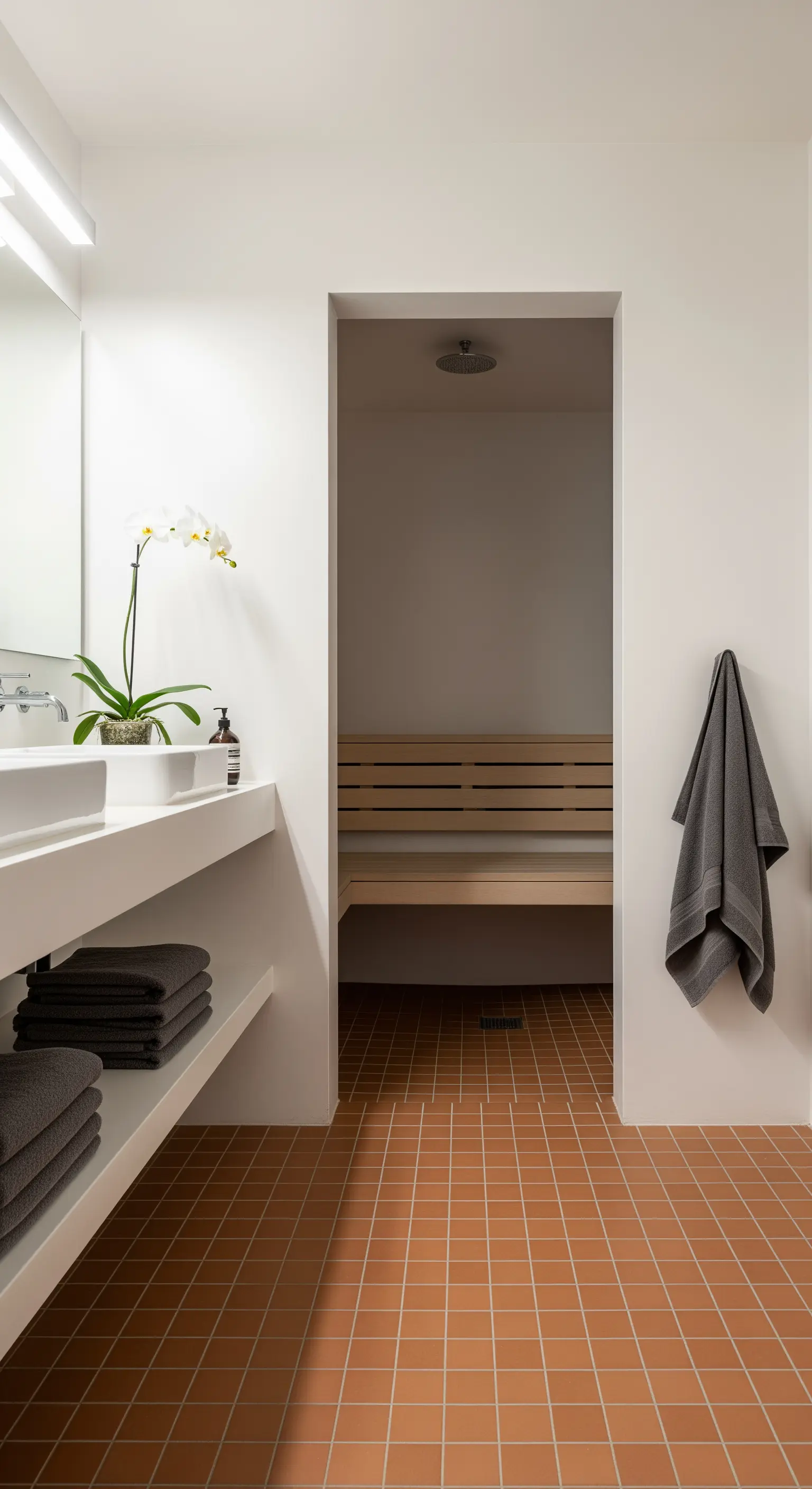 Bagno minimalista con pavimento in cotto che conduce a una sauna interna in legno chiaro.