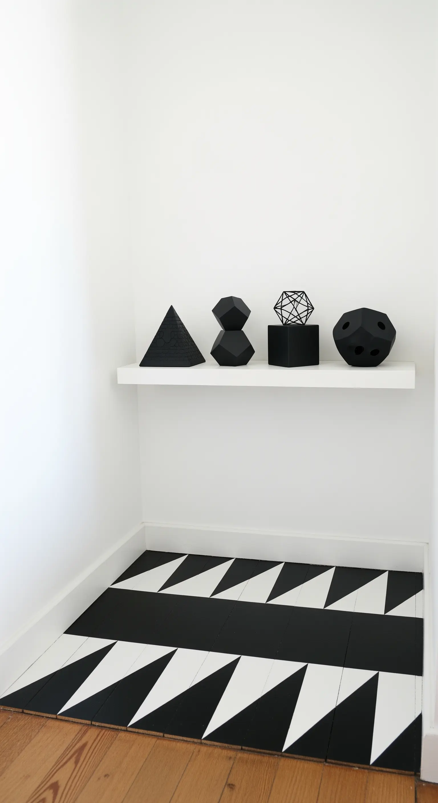 Angolo di un ingresso con pavimento in legno parzialmente dipinto con un motivo a triangoli bianchi e neri.