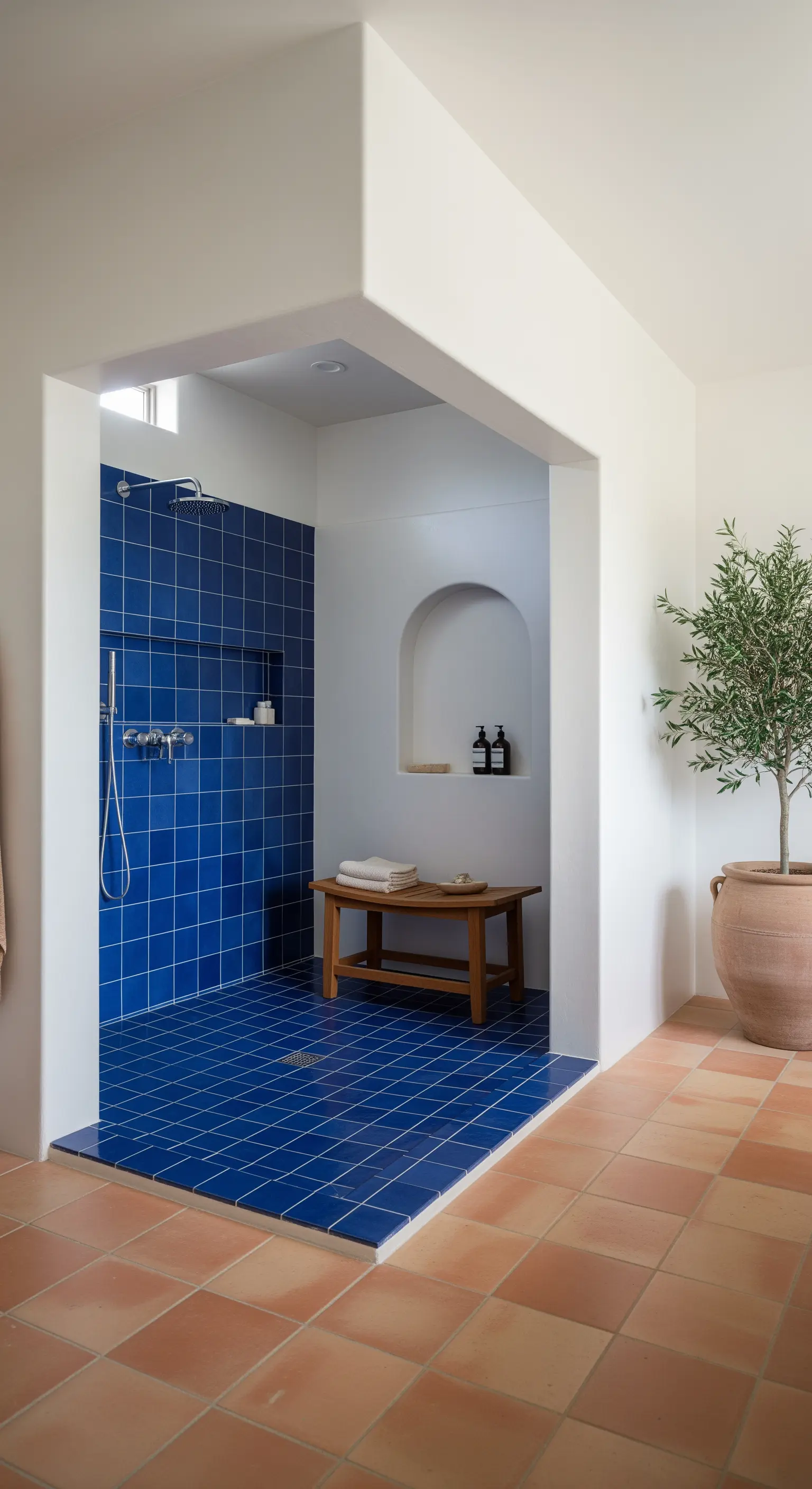 Doccia walk-in con piastrelle quadrate blu intenso e nicchia ad arco nella parete bianca.