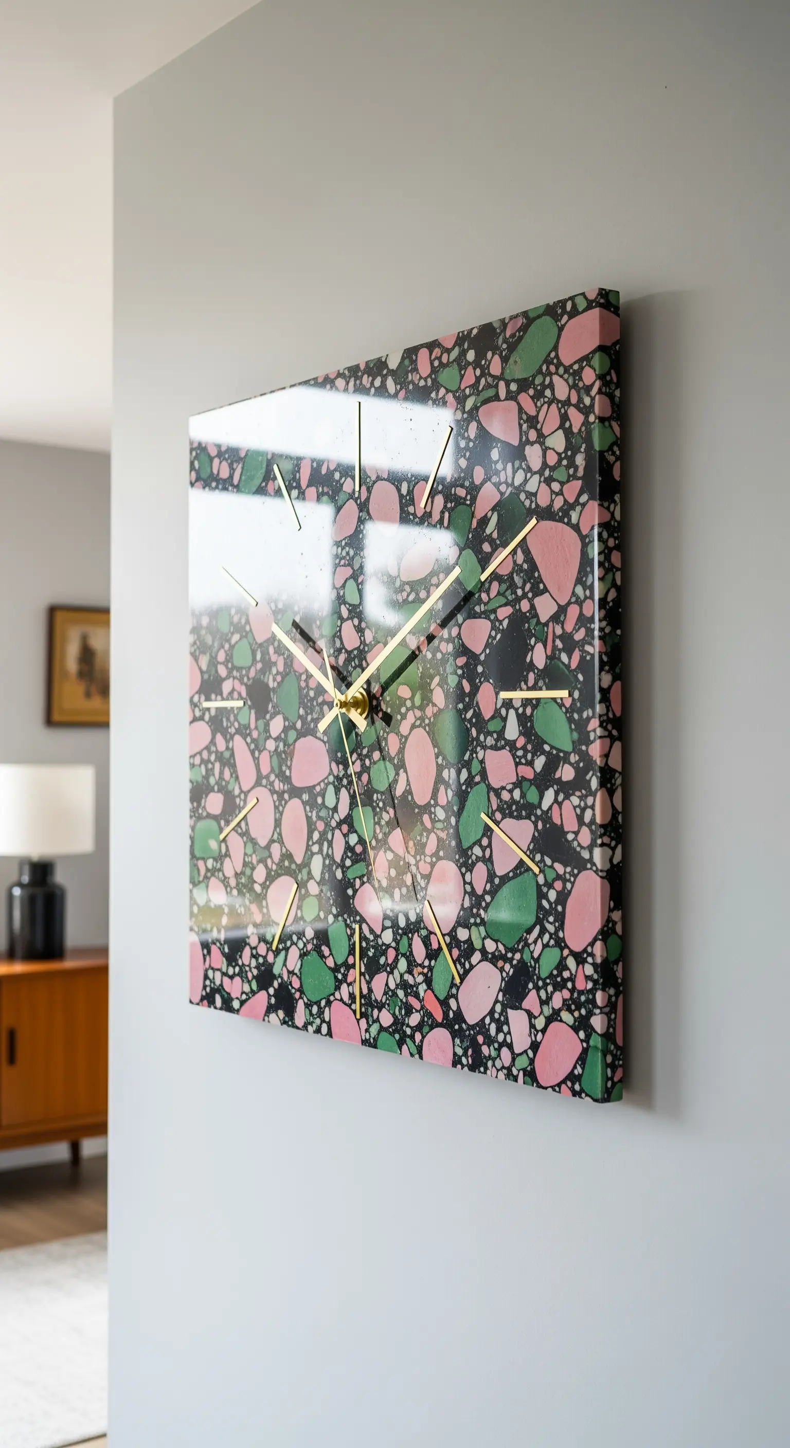 Orologio quadrato con motivo terrazzo nei toni del rosa, verde e nero, e lancette dorate.