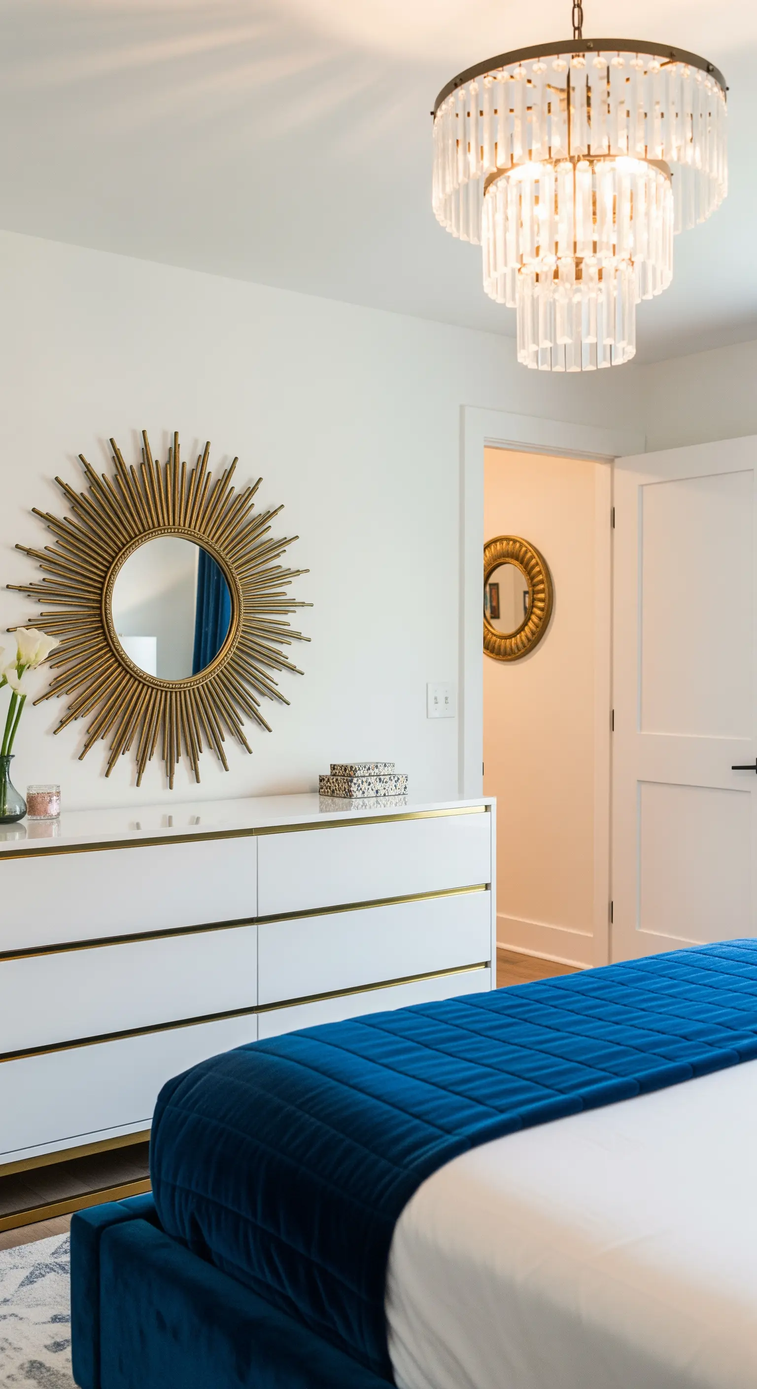 Cassettiera bianca con dettagli dorati, specchio a raggiera dorato e letto in velluto blu.