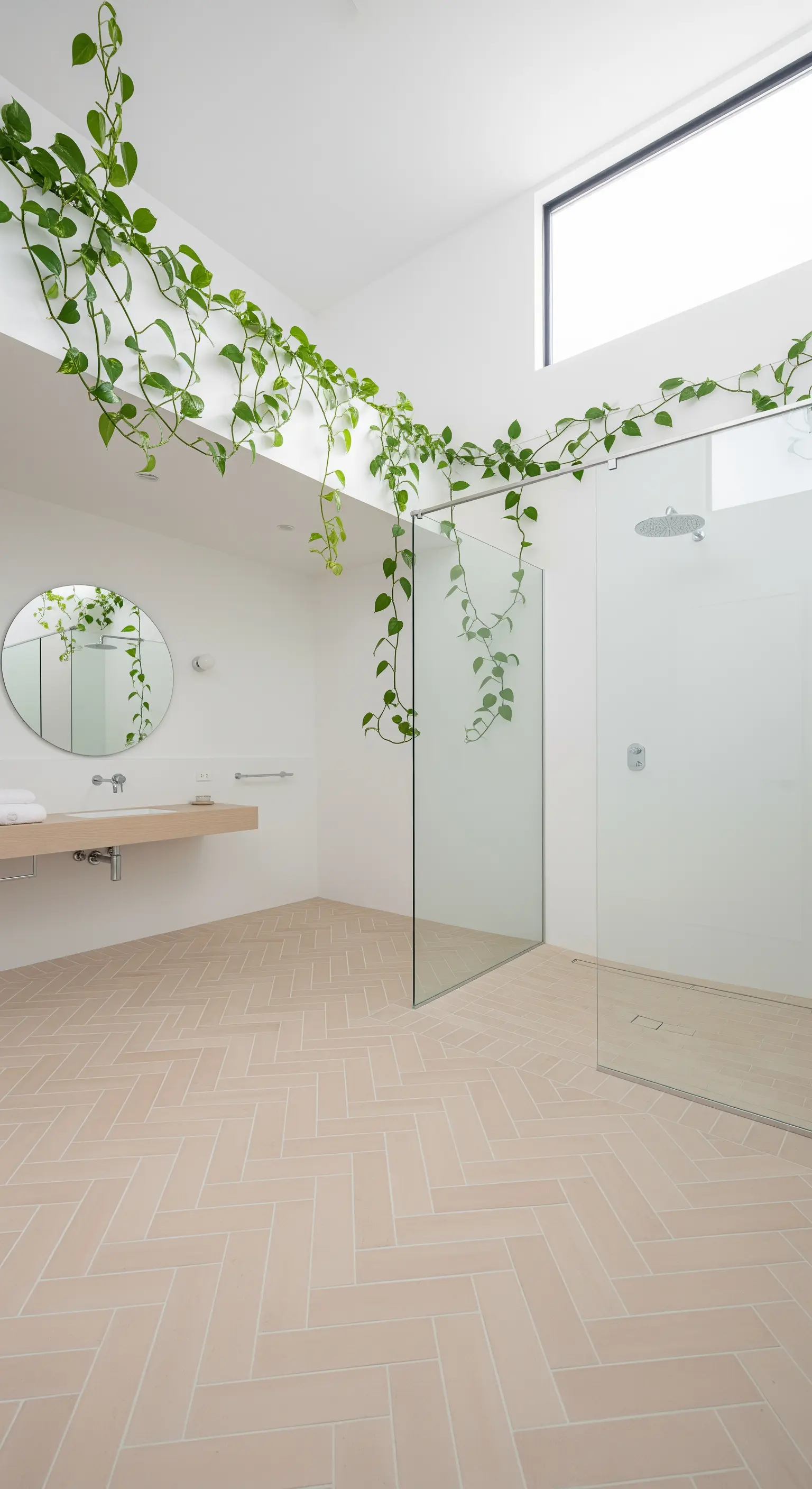 Bagno minimalista bianco e terracotta chiaro con una pianta di Pothos che si arrampica sulle pareti.