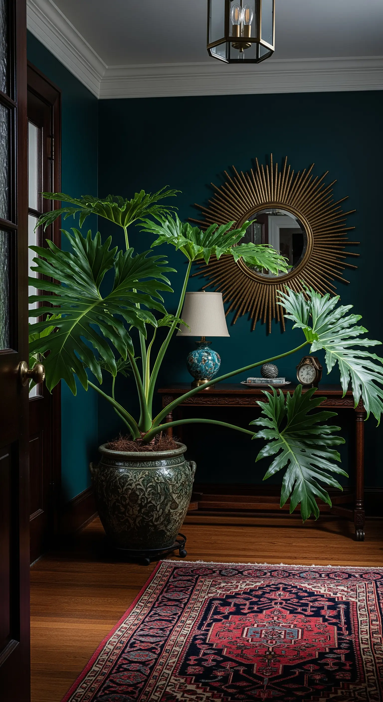Filodendro imponente contro una parete blu petrolio, accanto a una consolle con specchio dorato.