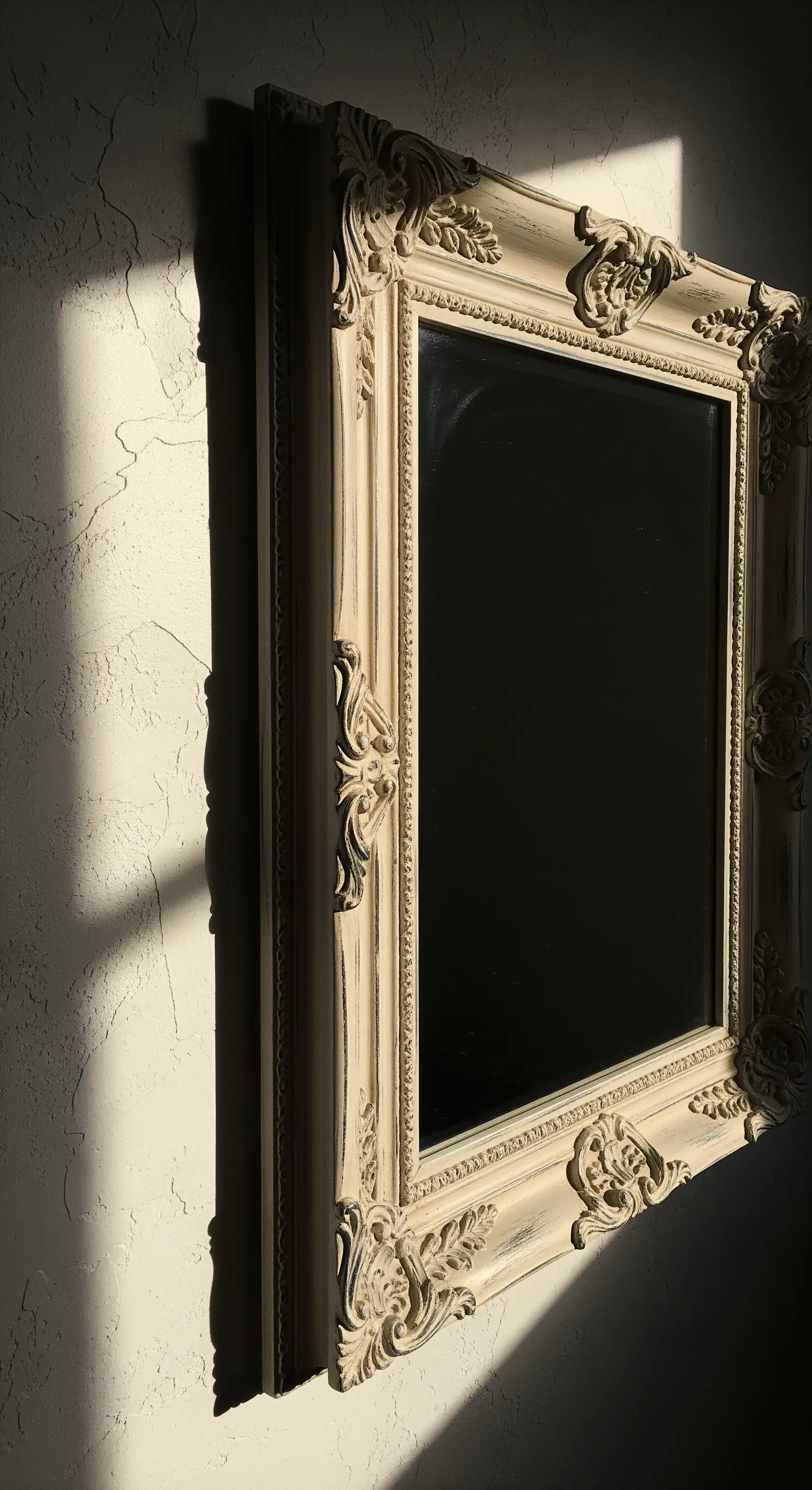 Cornice barocca color crema con finitura invecchiata, illuminata da una luce laterale intensa.