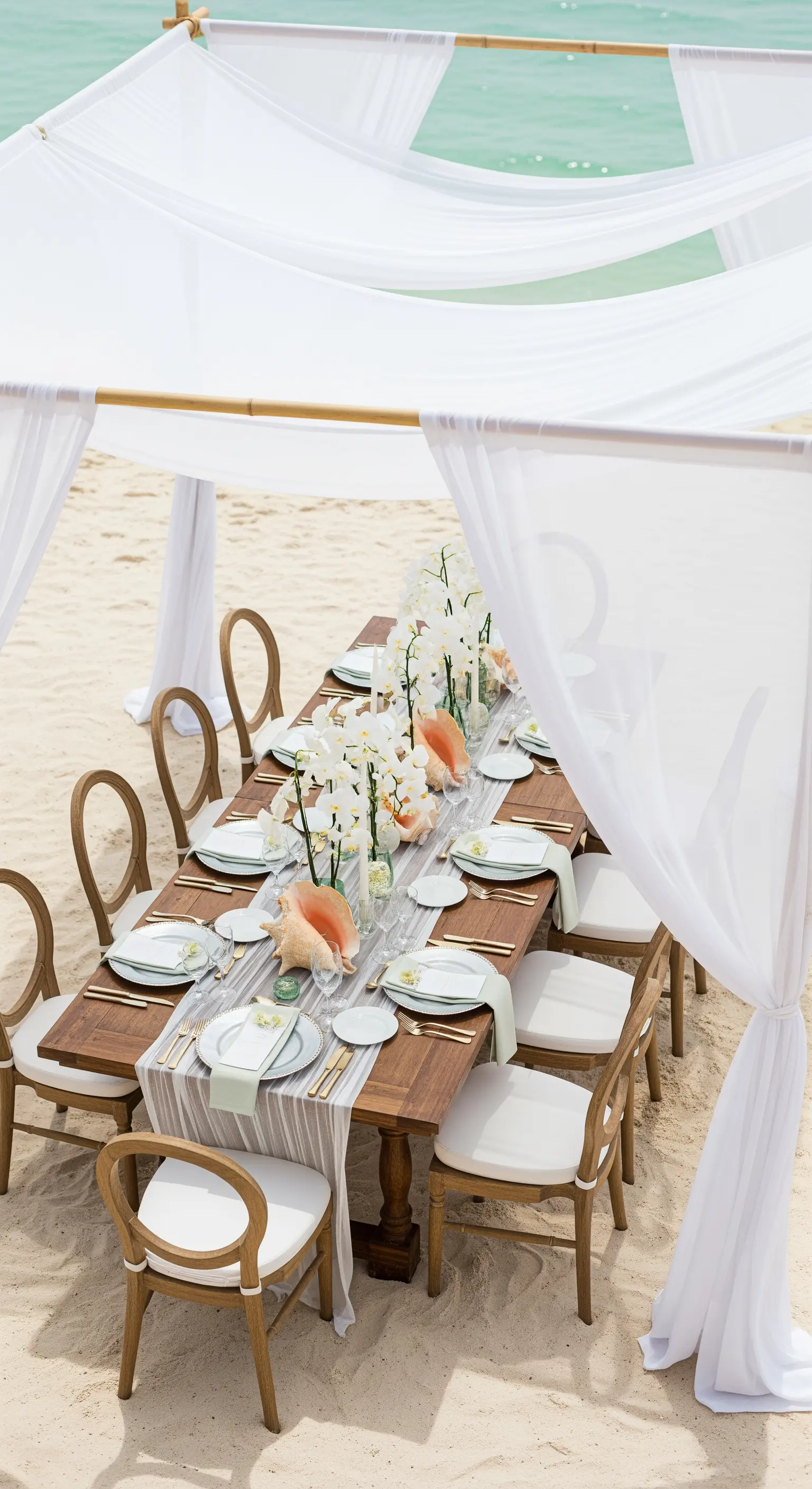 Tavola da pranzo elegante sulla spiaggia con sedie in legno e runner bianco.