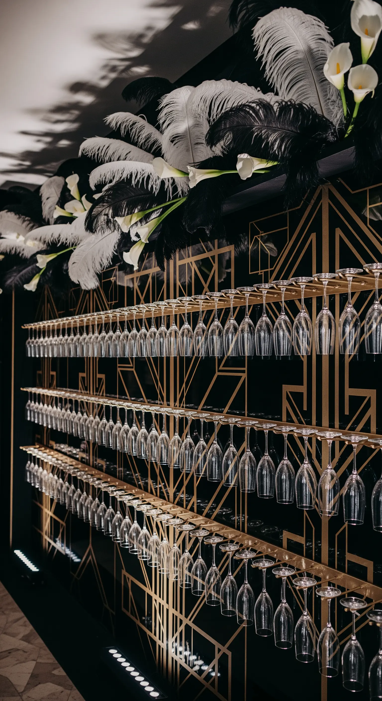 Prosecco wall in stile Art Déco nero e oro, decorato con piume bianche e calle.