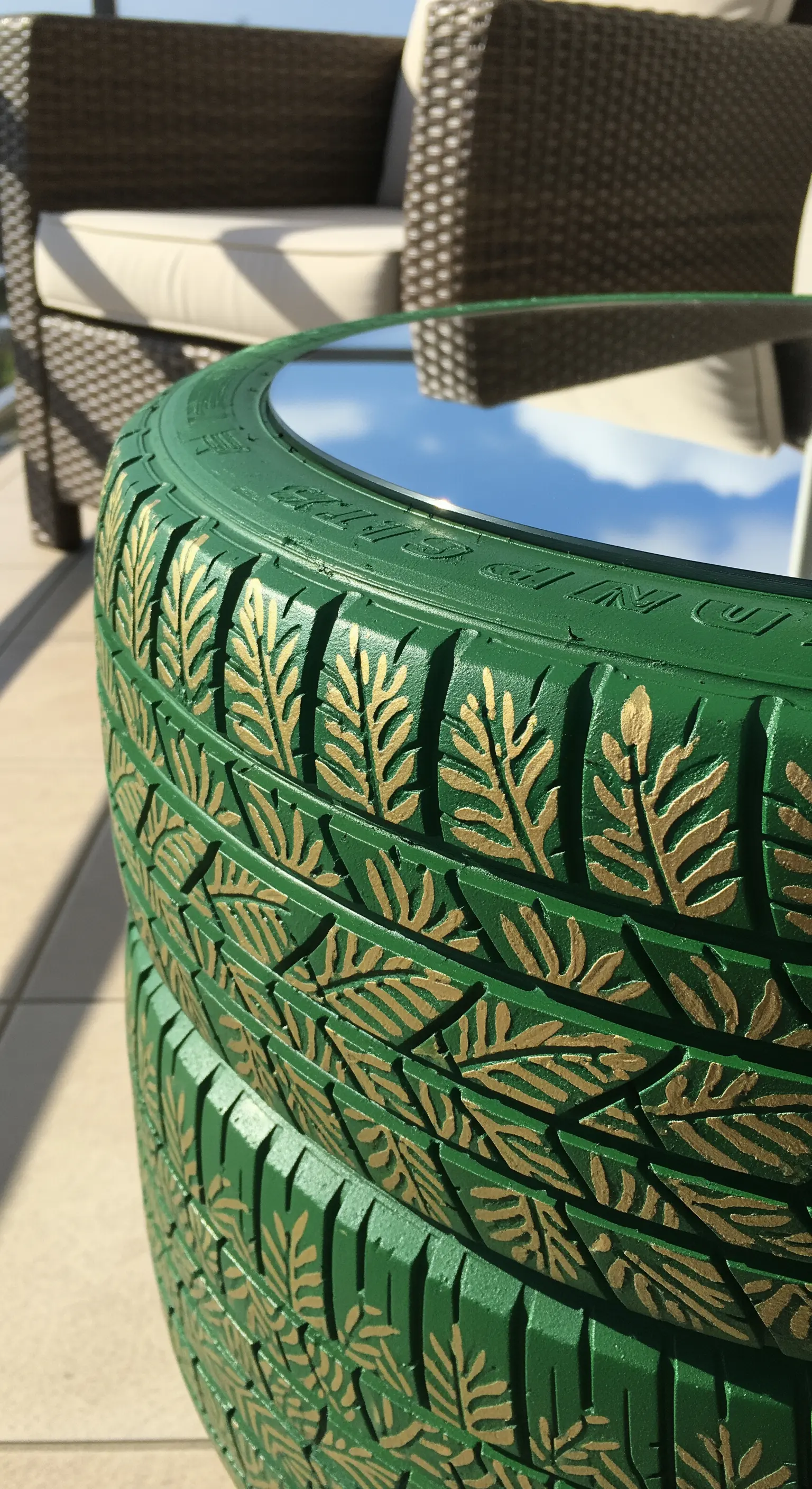 Tavolino verde scuro con motivi di foglie dorate dipinte sul battistrada del pneumatico.