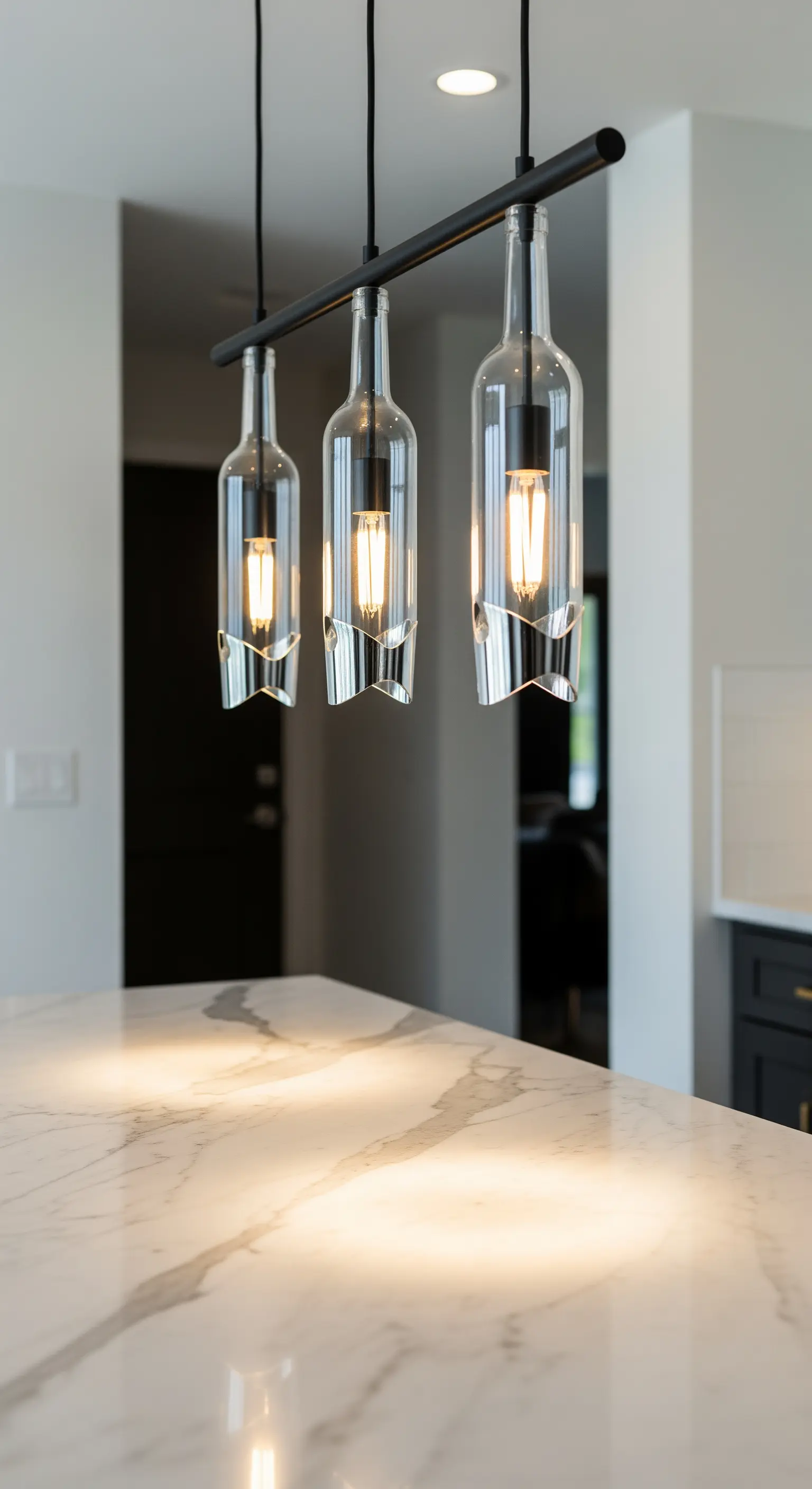 Lampadario lineare e moderno con tre bottiglie di vetro trasparente tagliate su un'isola di marmo.