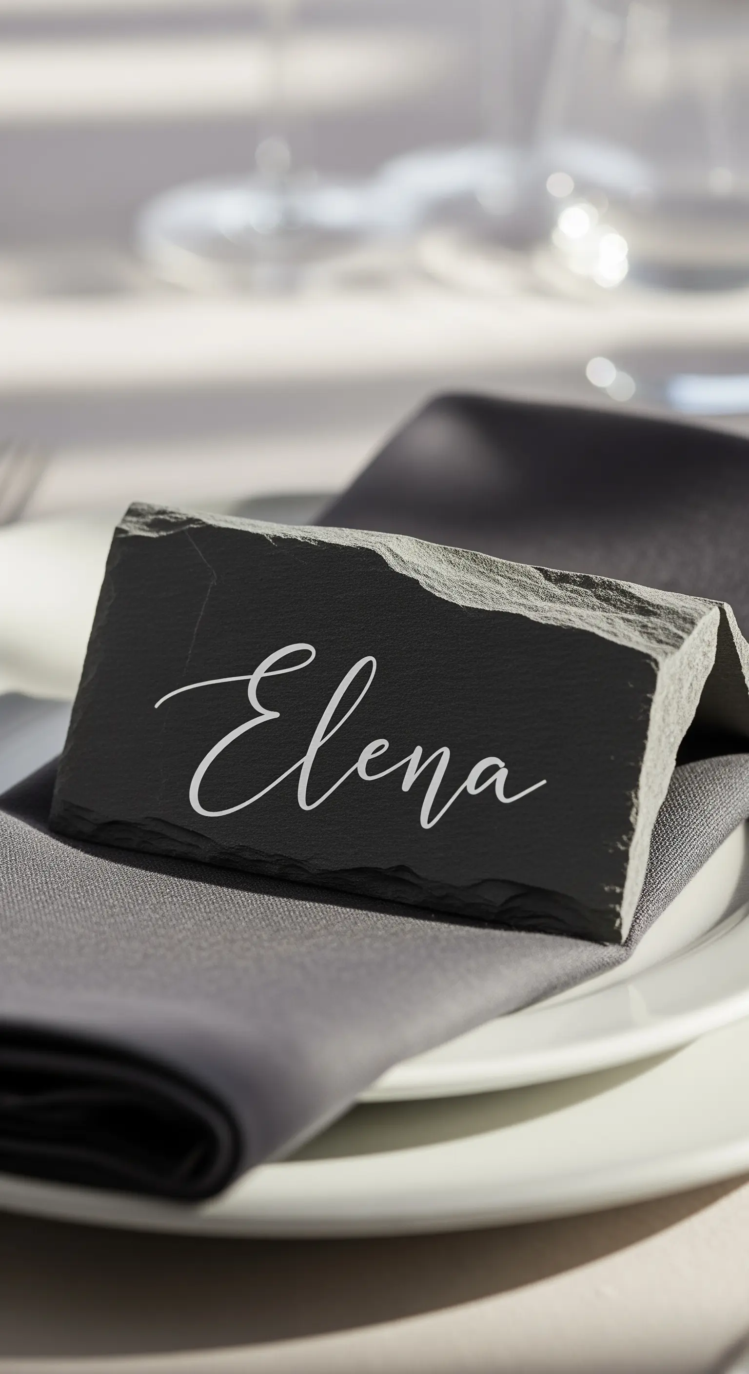 Segnaposto minimalista in ardesia scura con nome scritto in calligrafia bianca.