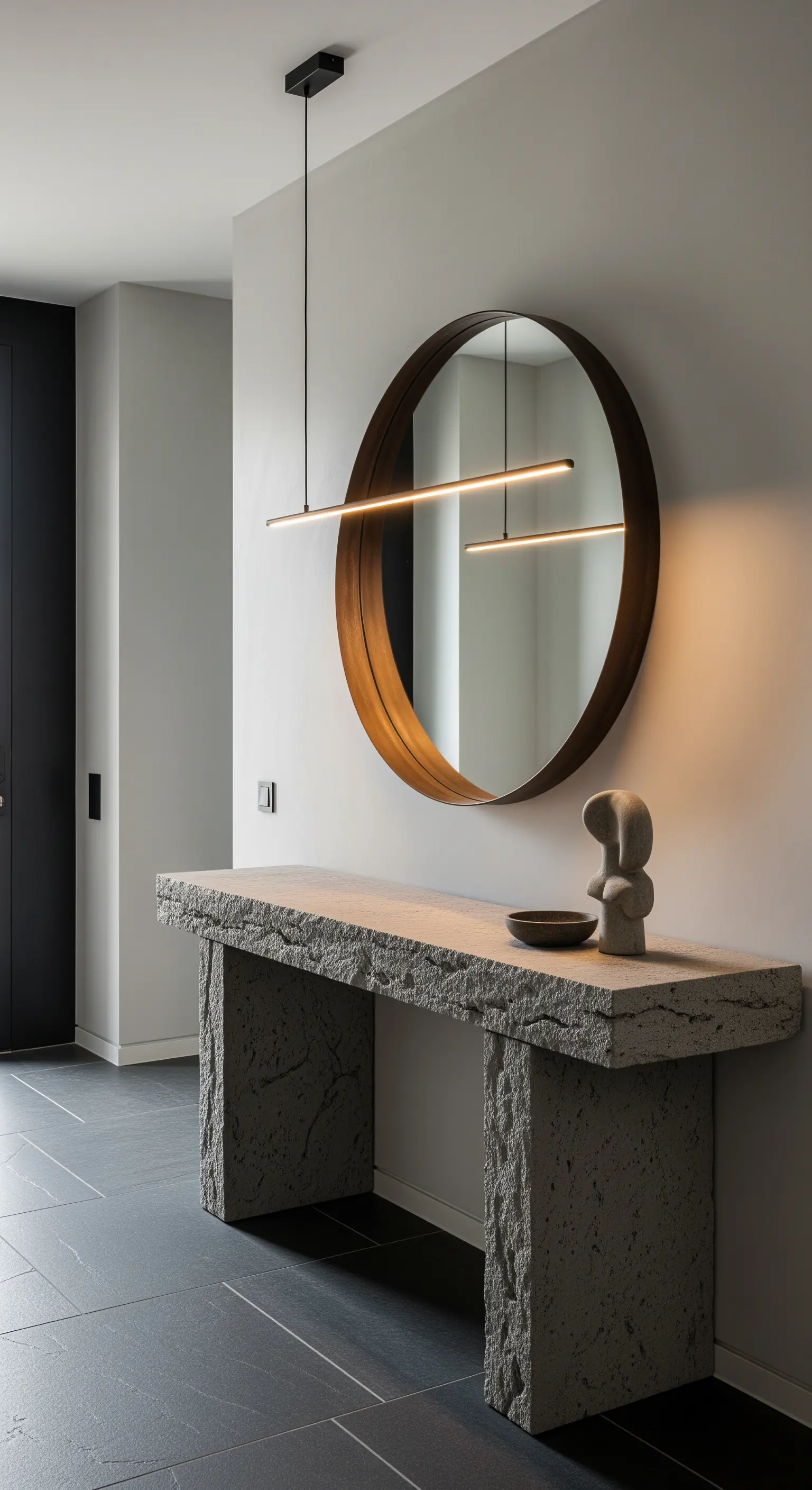 Consolle in pietra grezza con lampada a sospensione lineare a LED e specchio con cornice metallica.