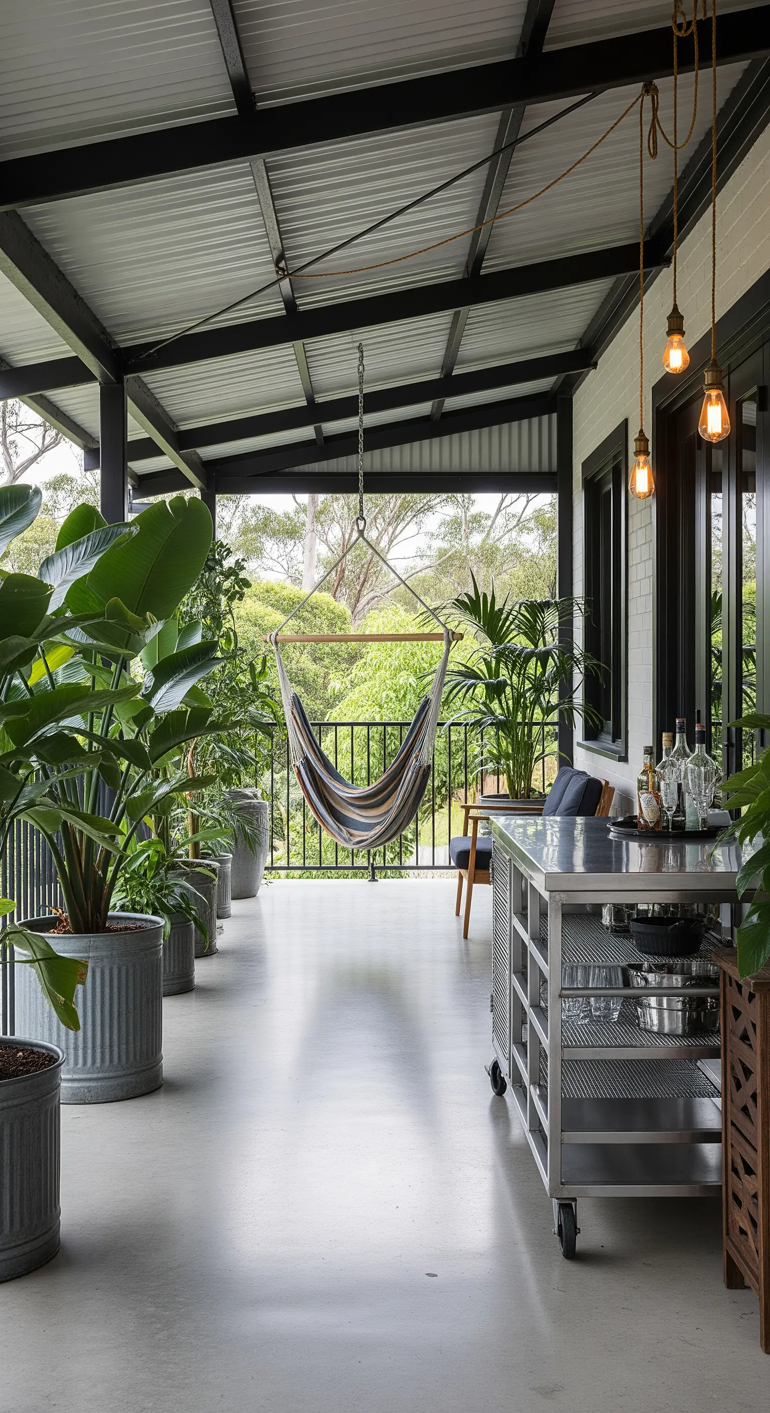 Portico con pavimento in cemento, carrello bar in acciaio, grandi piante in vasi di zinco e amaca