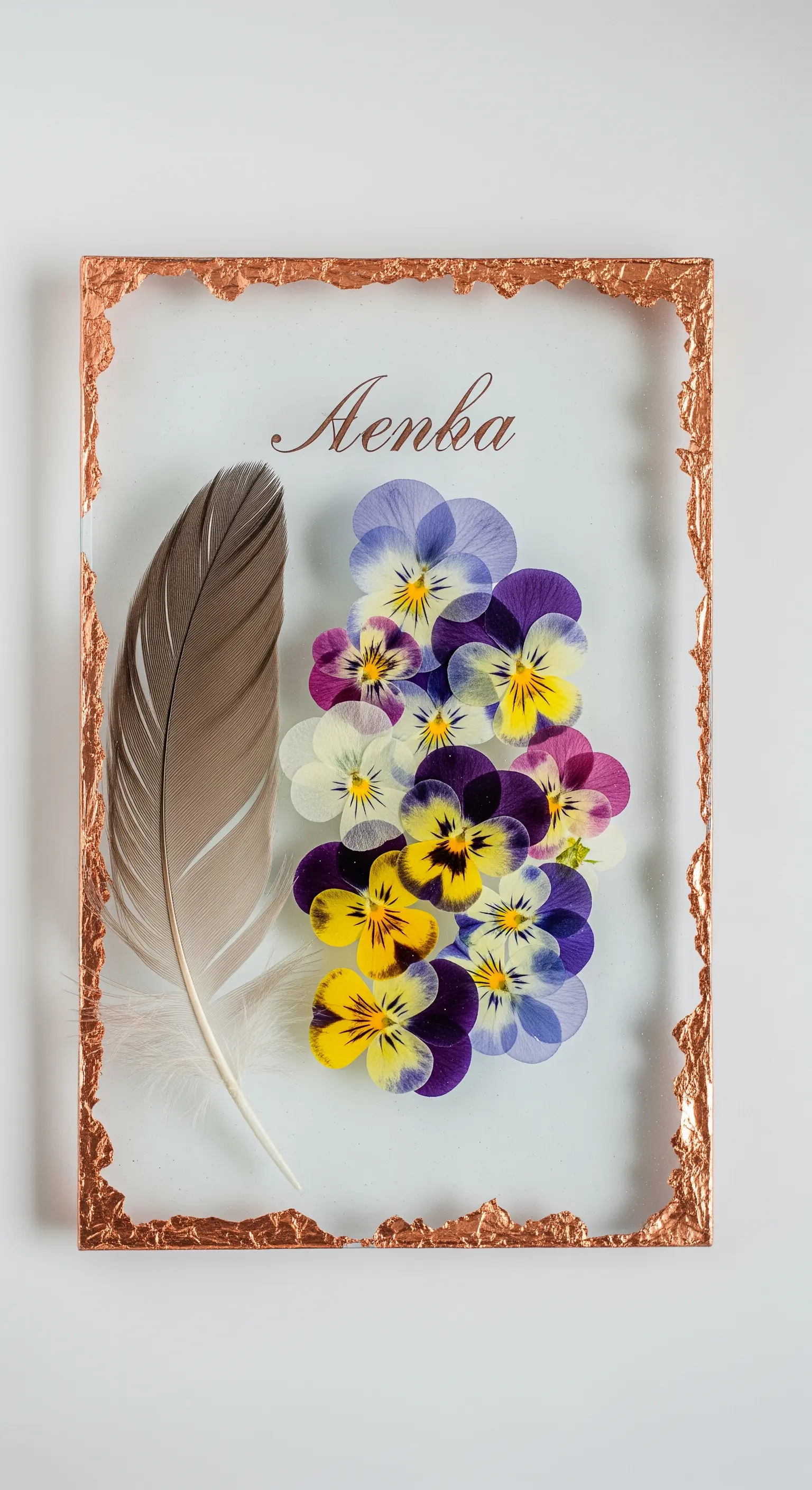 Segnaposto con fiori pressati e piuma racchiusi in una cornice di vetro e rame.