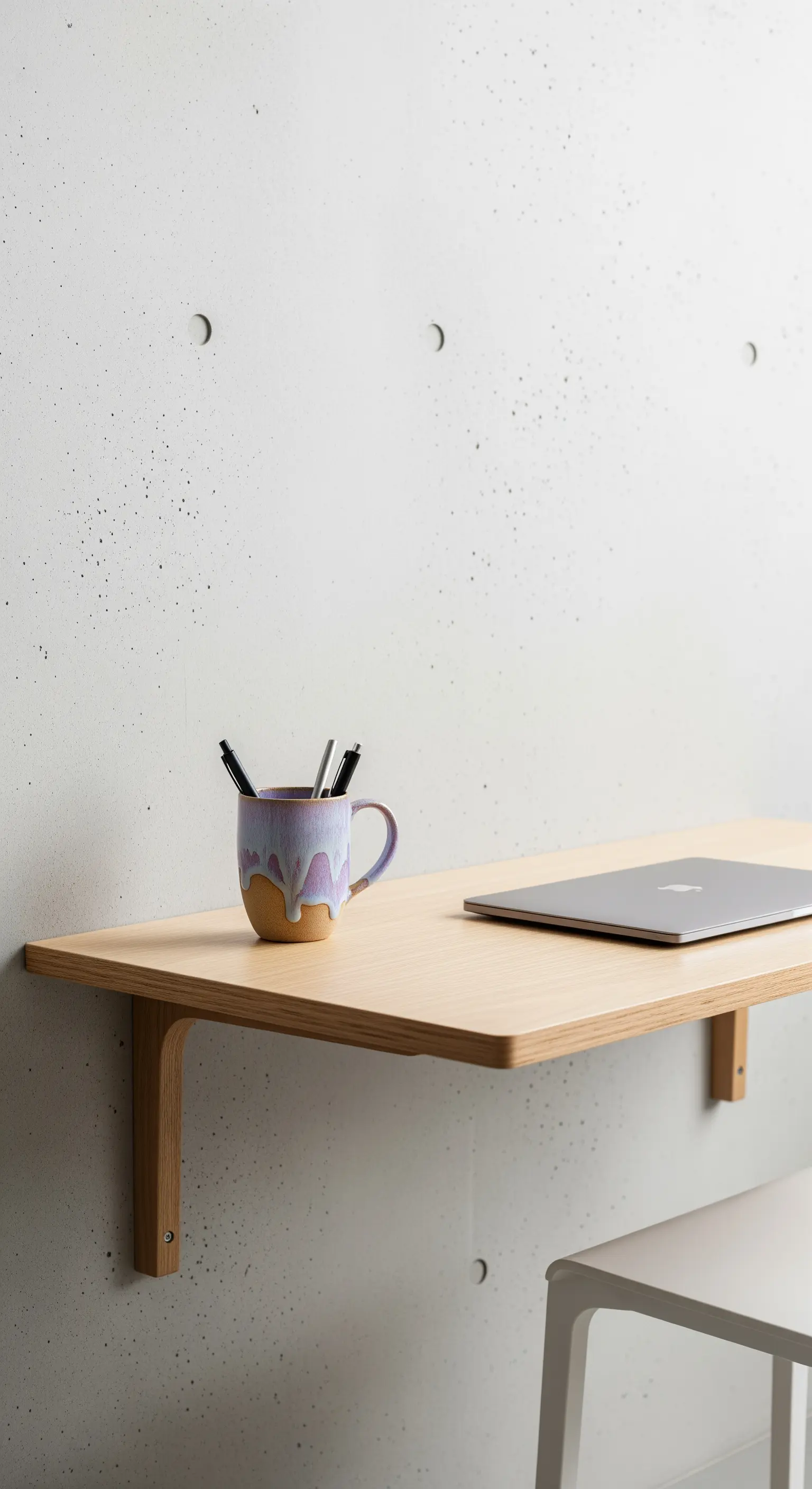 Mensola-scrivania in legno chiaro fissata a una parete di cemento grezzo.