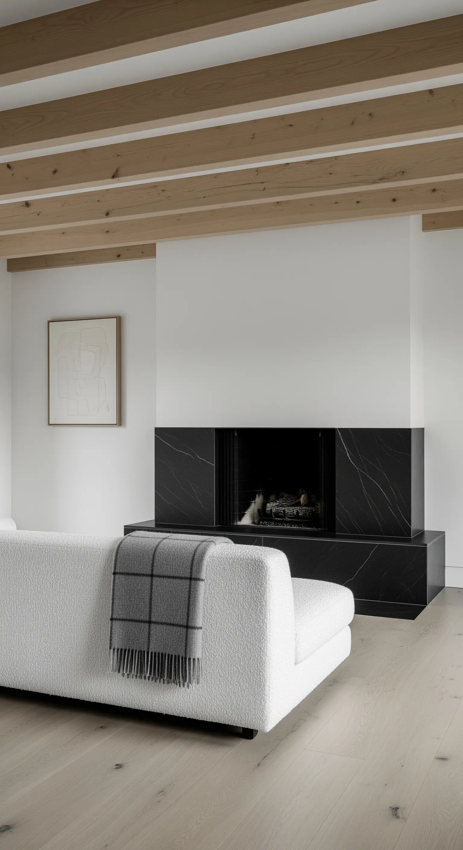 Salotto minimalista con camino in marmo nero, divano bouclé bianco e travi a vista