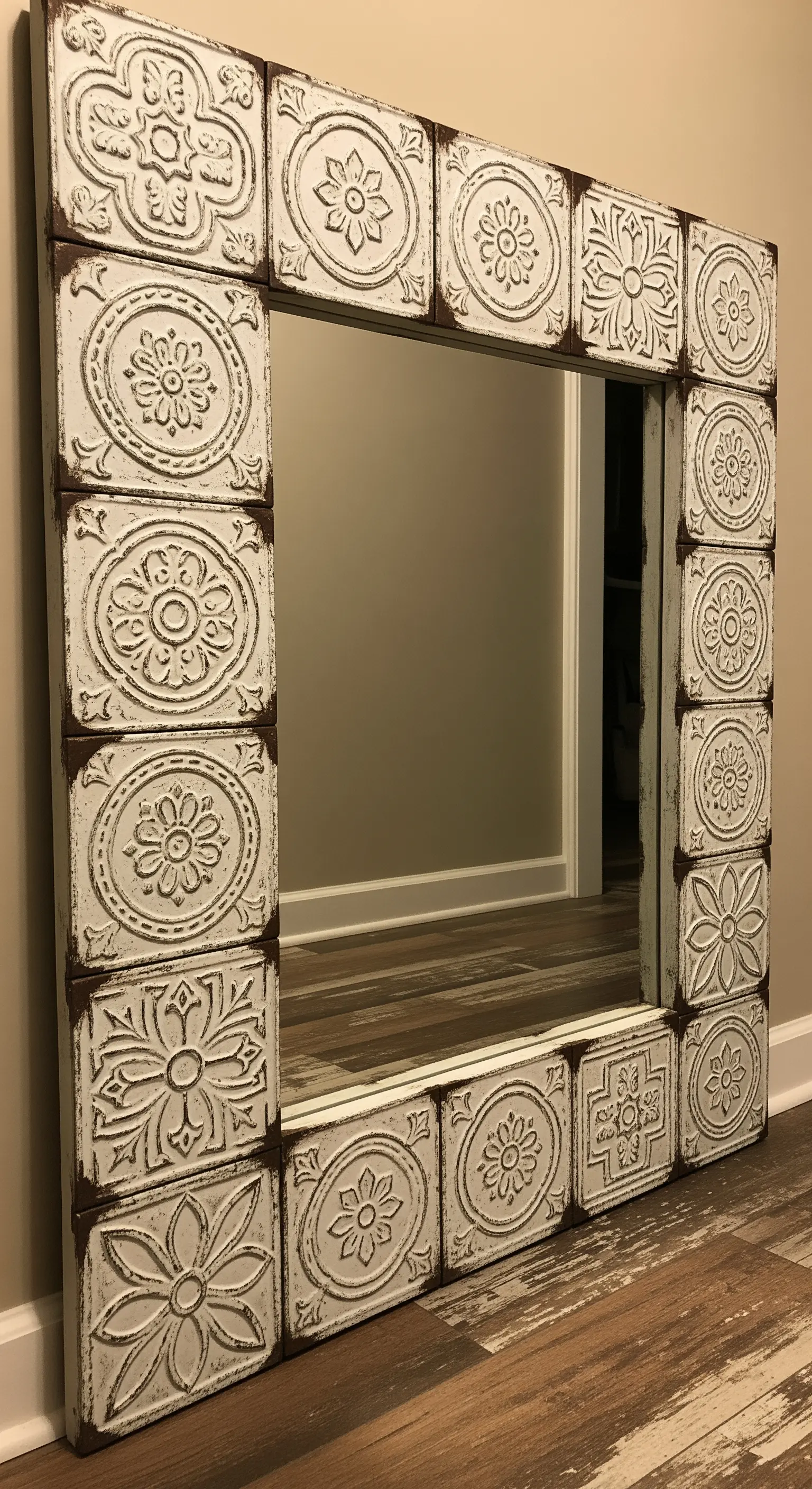 Specchio quadrato con cornice fatta di piastrelle di latta bianca con motivi floreali in rilievo.