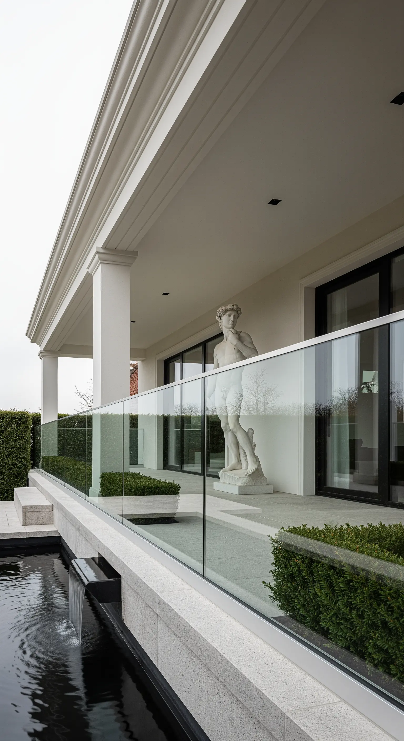 Terrazza moderna con balaustra in vetro, statua classica e un piccolo canale d'acqua.