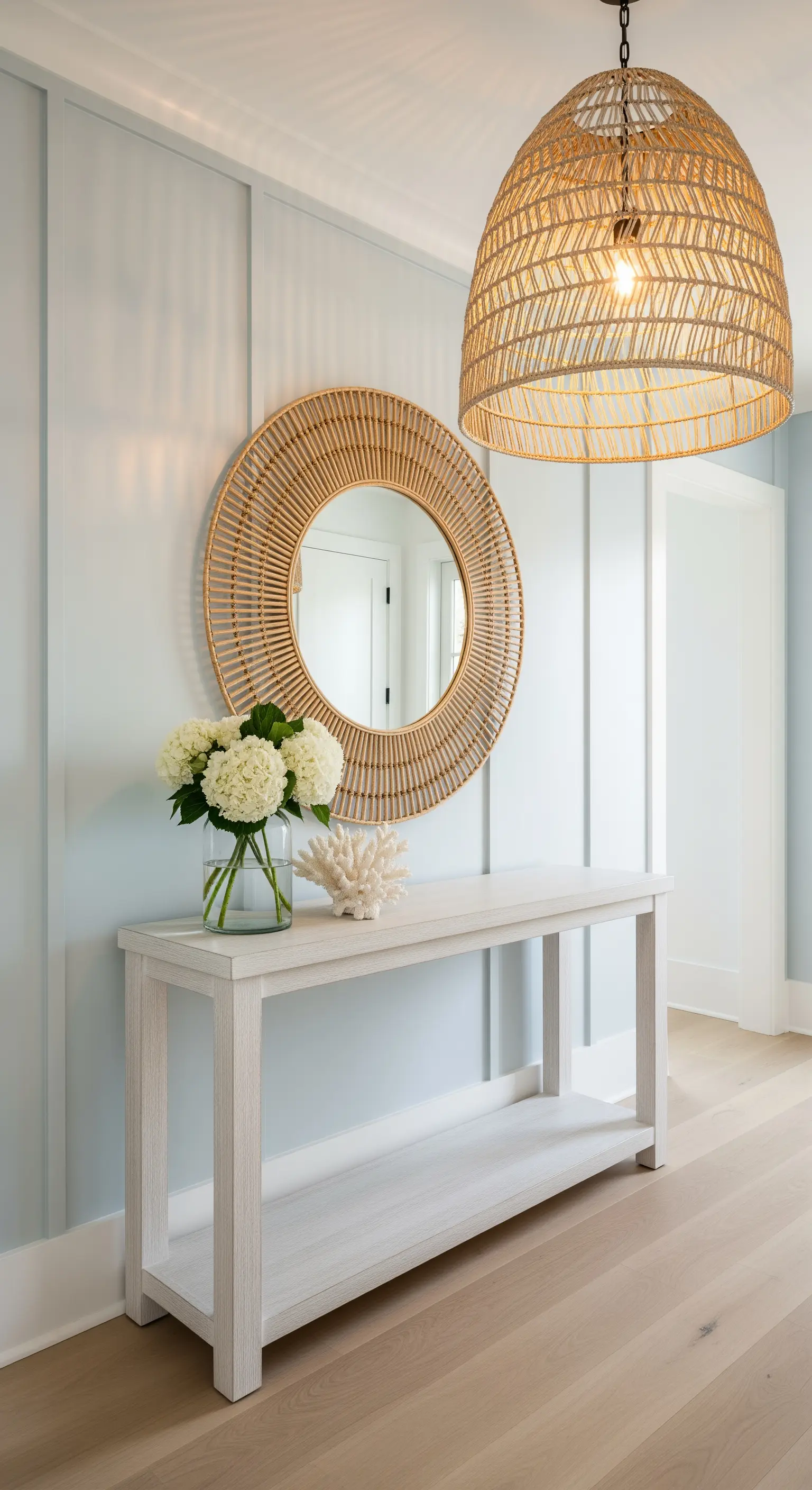 Ingresso in stile costiero con boiserie azzurra, consolle bianca e specchio in rattan.