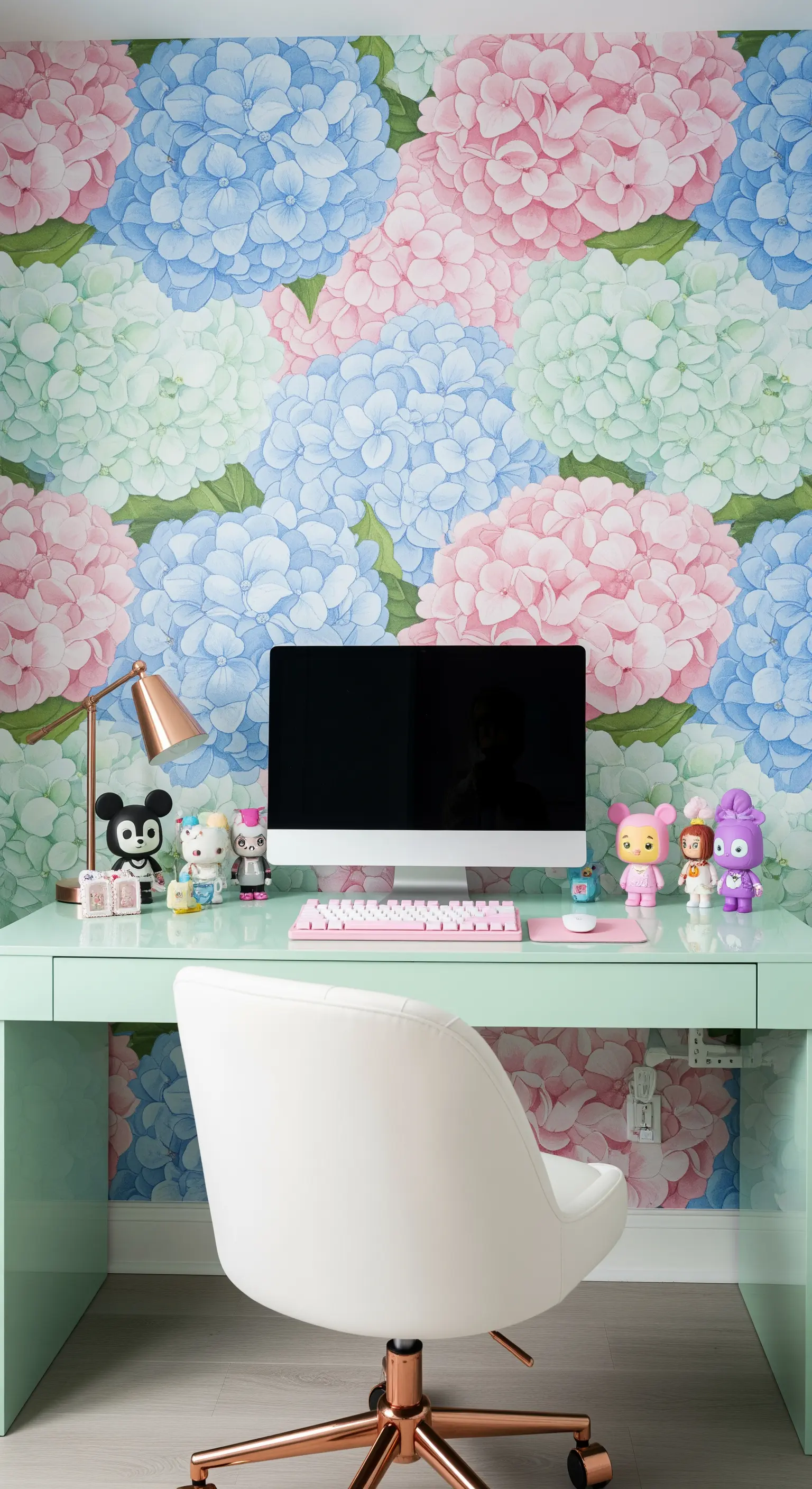 Scrivania verde menta con sedia bianca e dettagli ramati davanti a una carta da parati con ortensie.