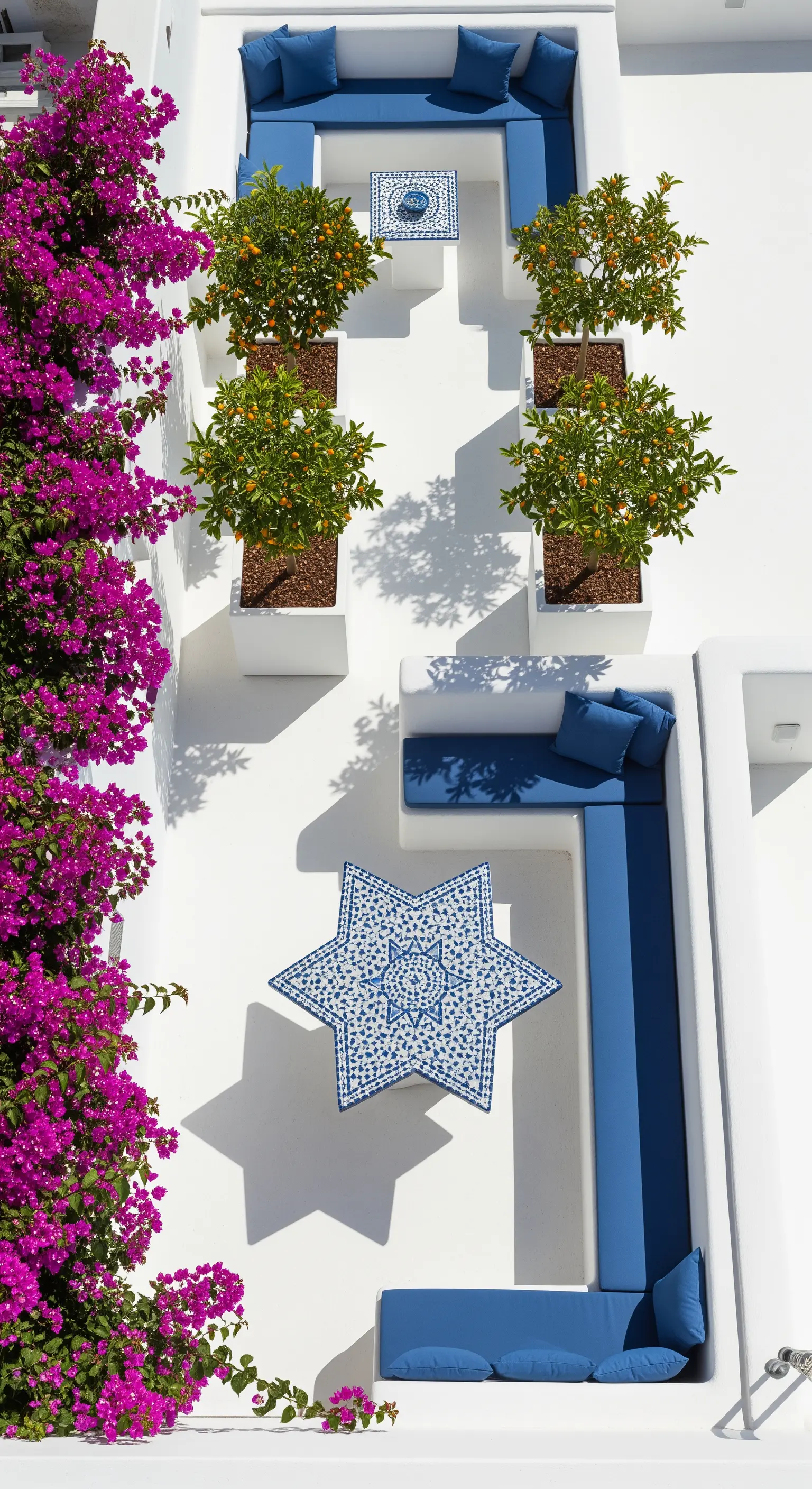 Terrazza bianca con divani in muratura, cuscini blu cobalto, piante di agrumi e bouganville.