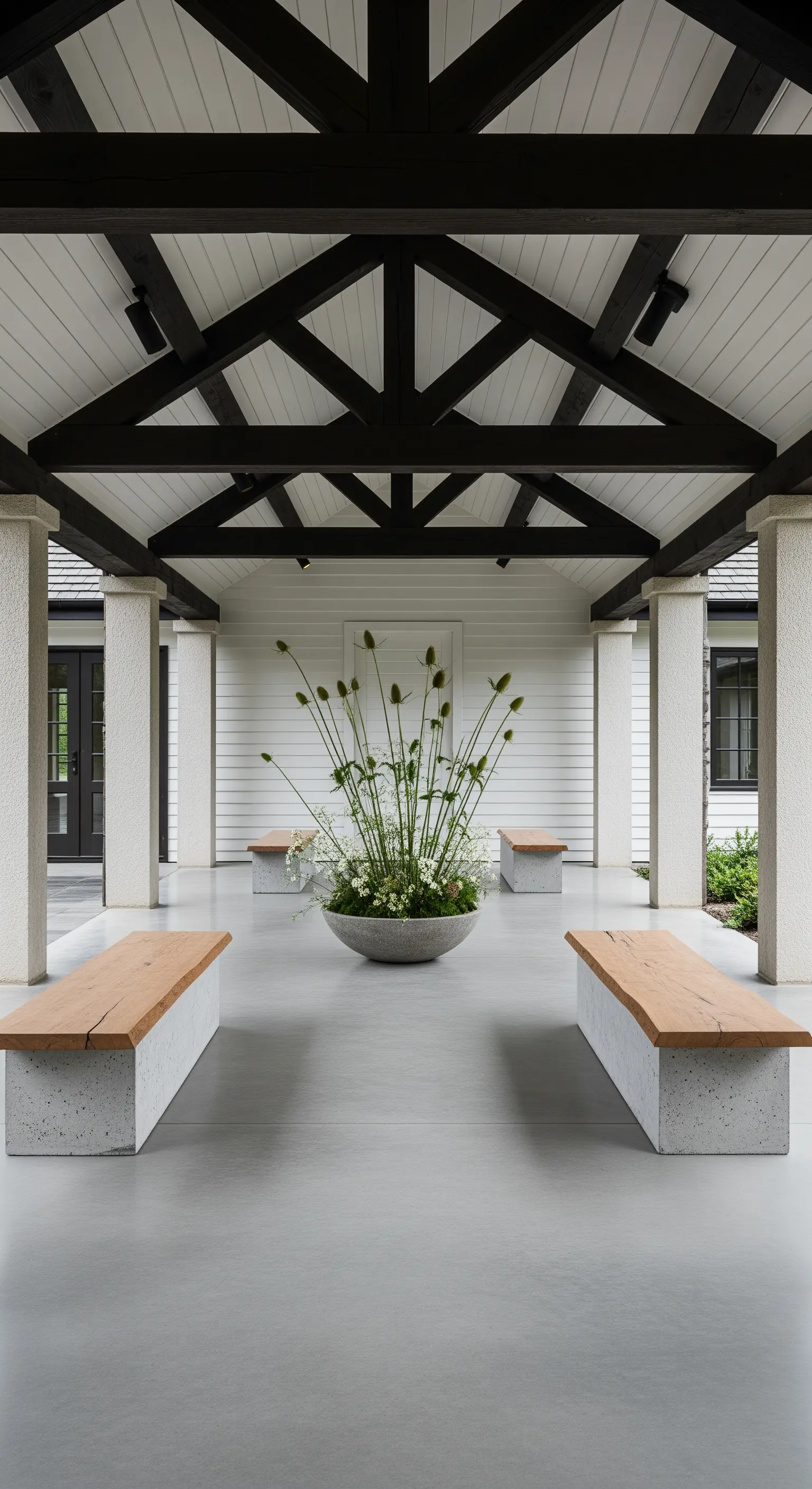 Portico moderno con travi nere, colonne bianche e panche in cemento e legno.