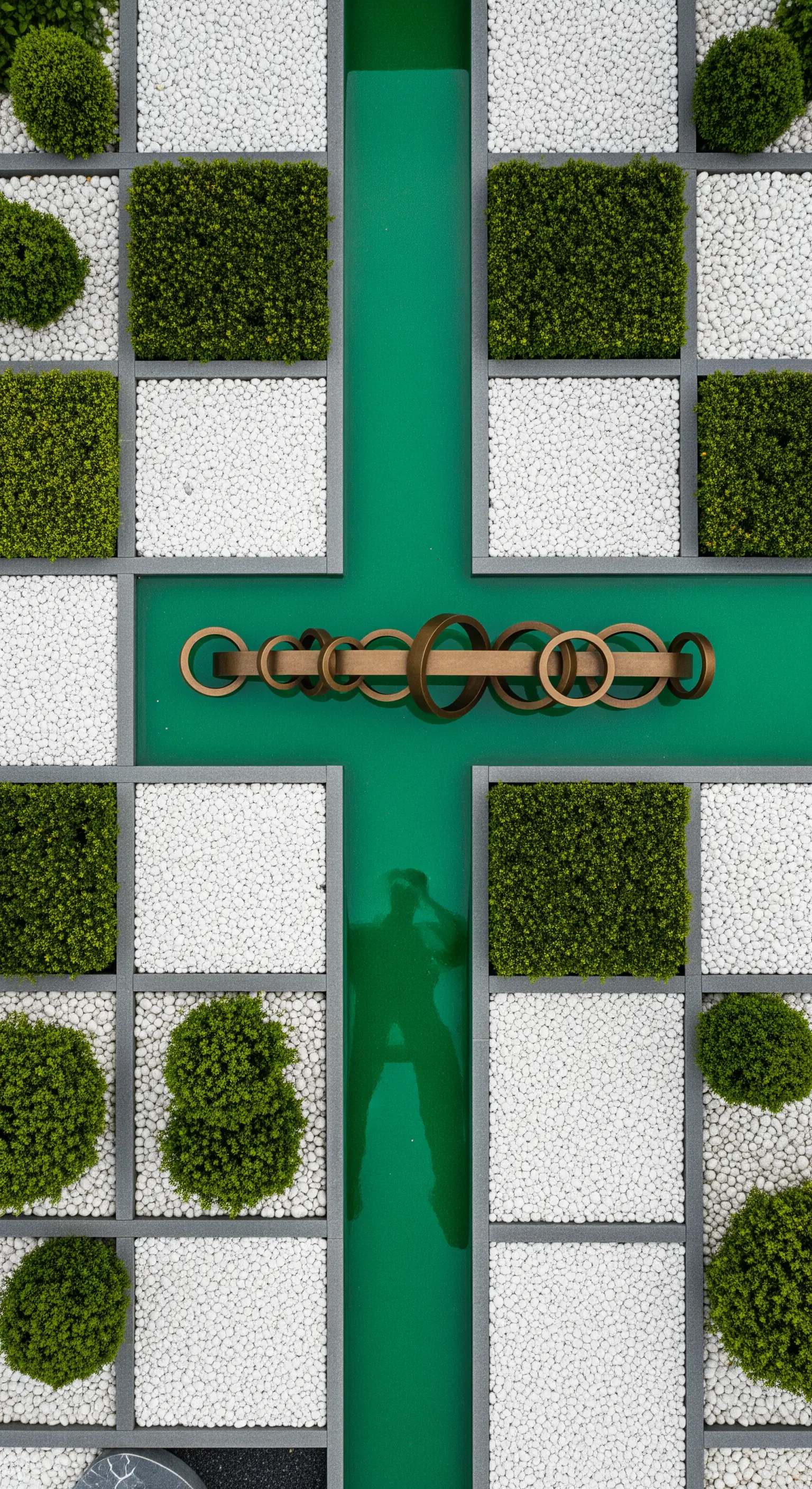 Vista aerea di un giardino geometrico con pavimentazione in resina verde e scultura in bronzo.