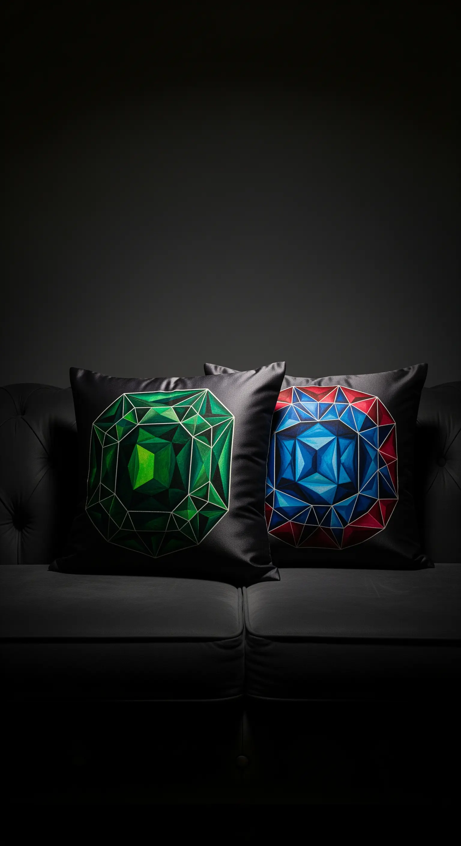 Due cuscini in raso nero con gemme geometriche dipinte in verde e blu su un divano scuro.