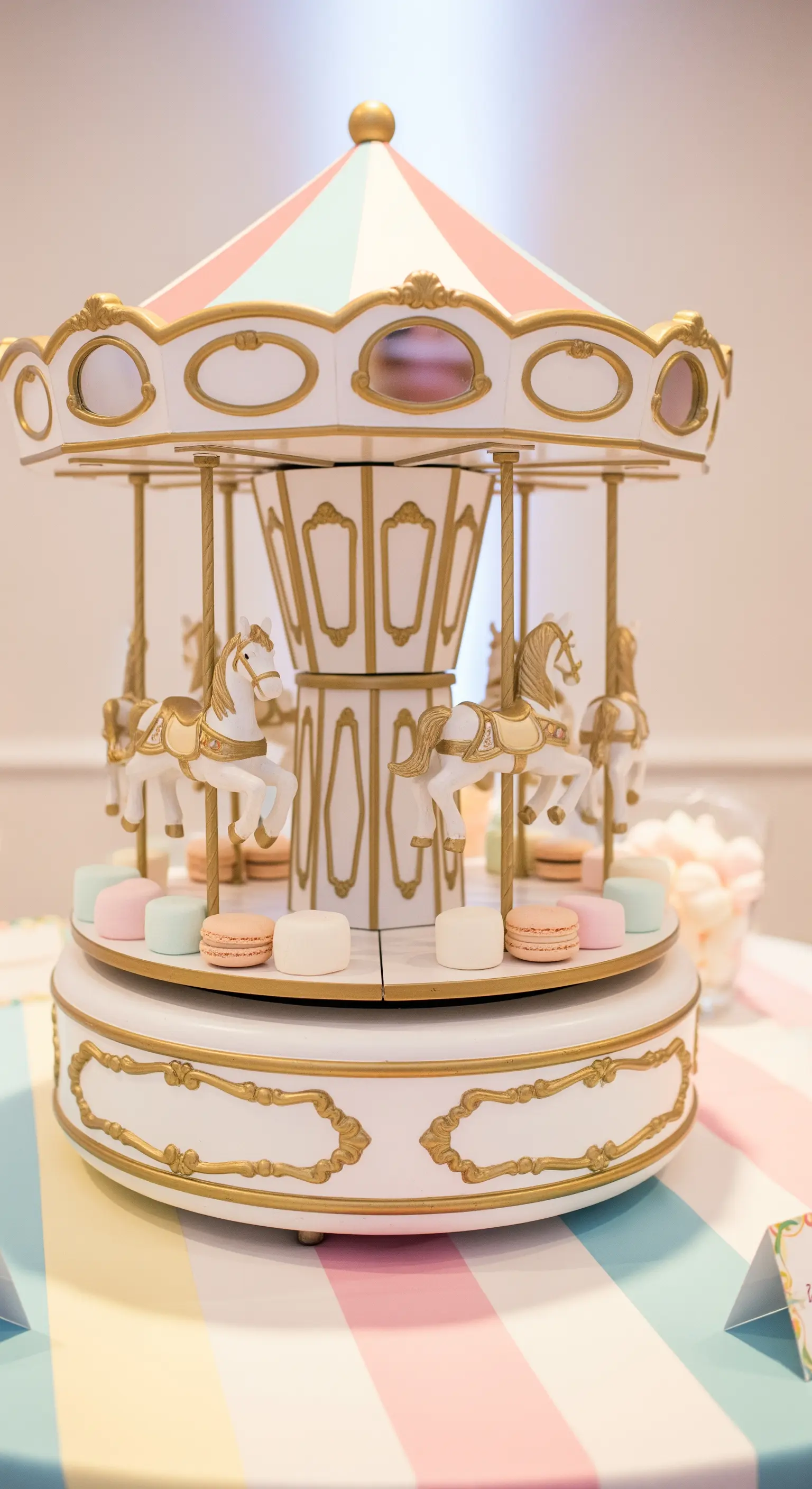Centrotavola a forma di giostra carosello con cavalli bianchi e oro, circondata da dolci pastello.